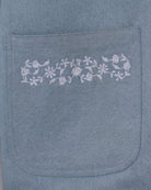 Close-up of white floral embroidery on jean-style front pocket of a light blue jacket