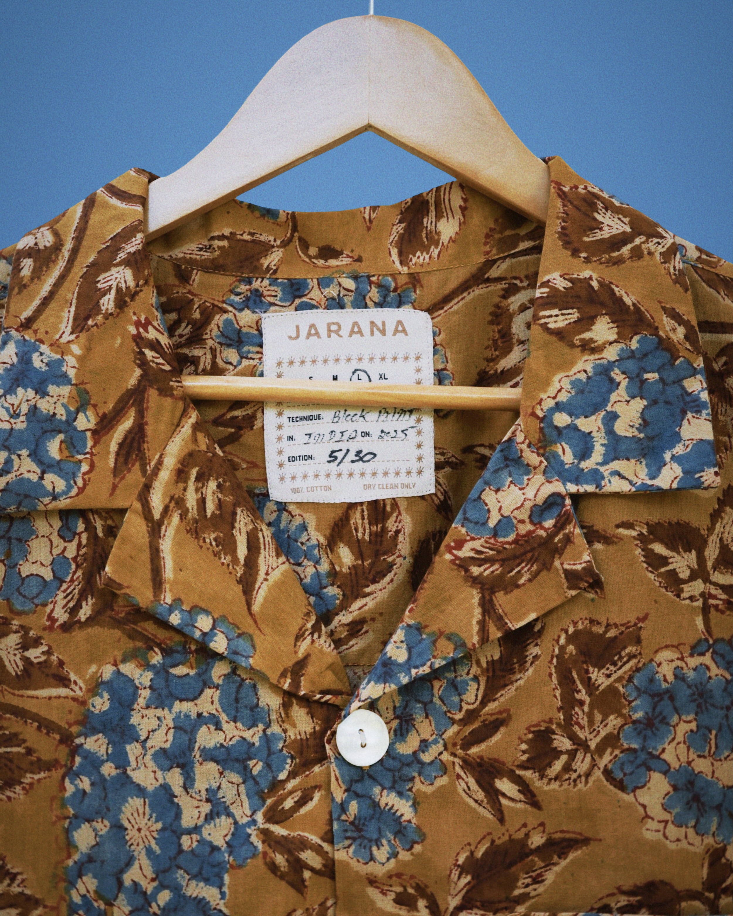 Close view of blue hydrangea and brown leaf block print on retro-toned cotton shirt with white button.