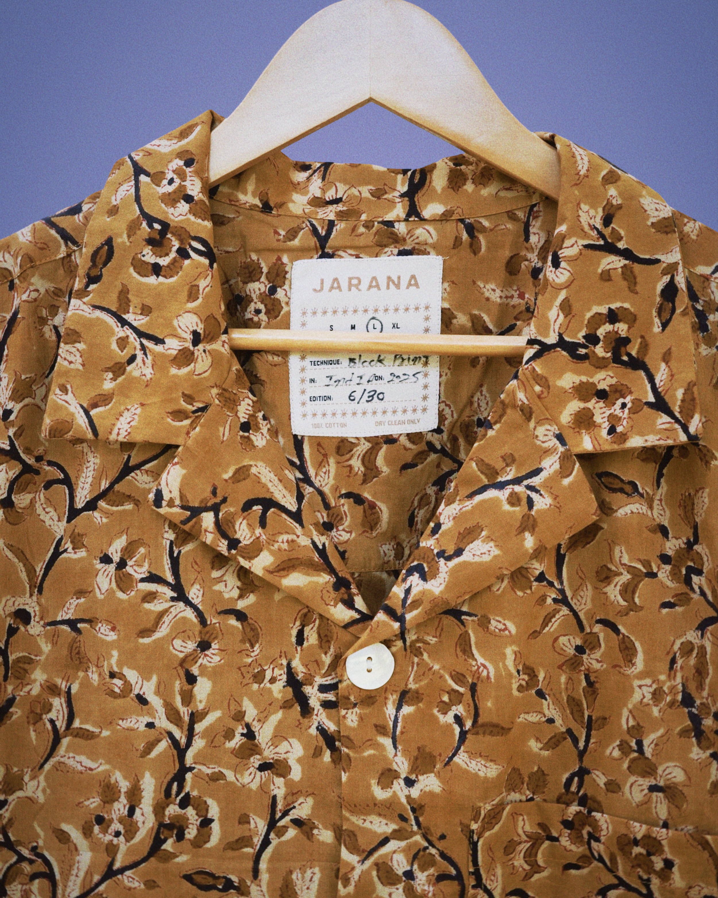 Close-up of brown cotton shirt with fine sepia floral block print and shell button, hanging on hanger.