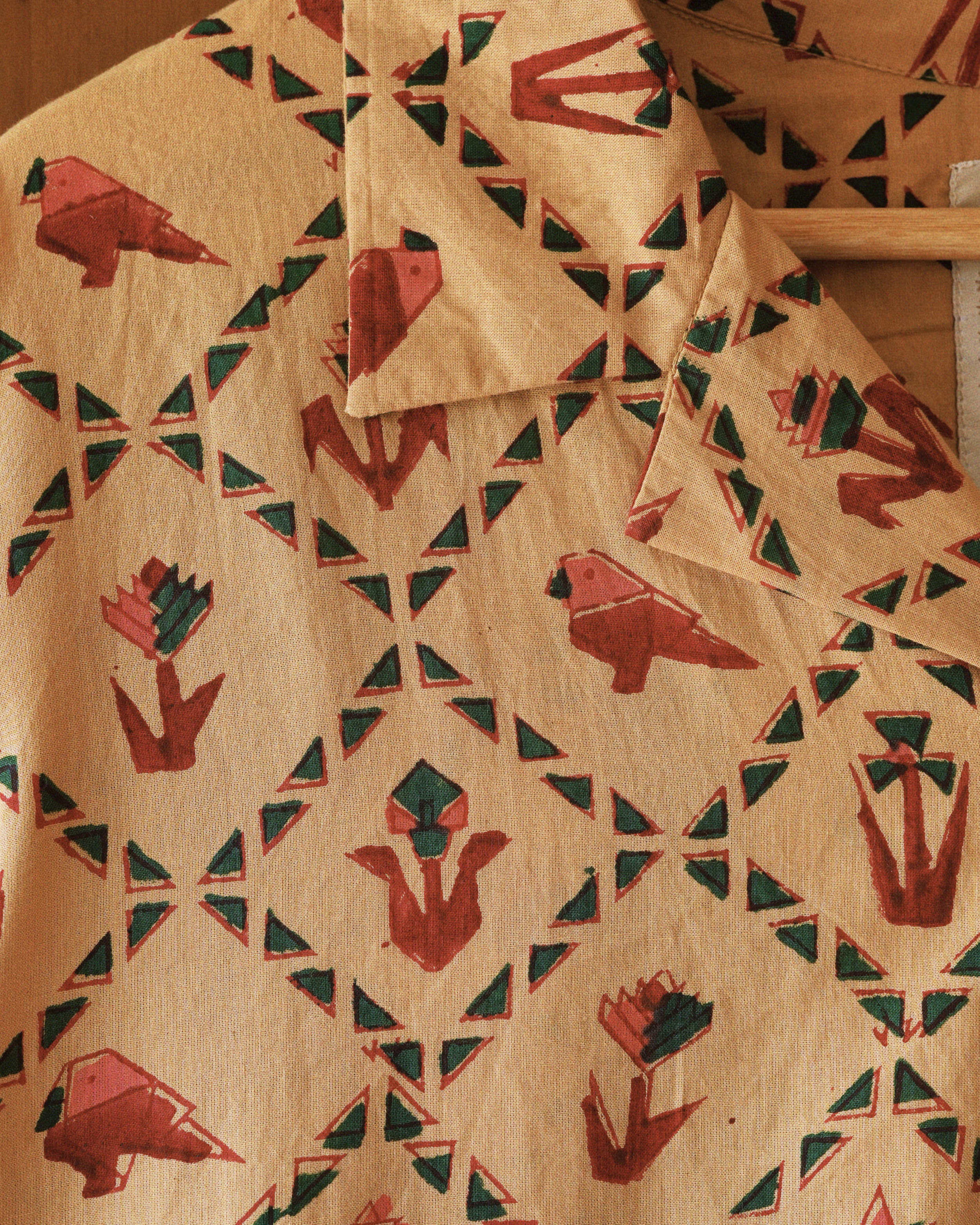 Close-up of hand block-printed pattern with red parrots, green triangles, and abstract flowers on beige cotton fabric.