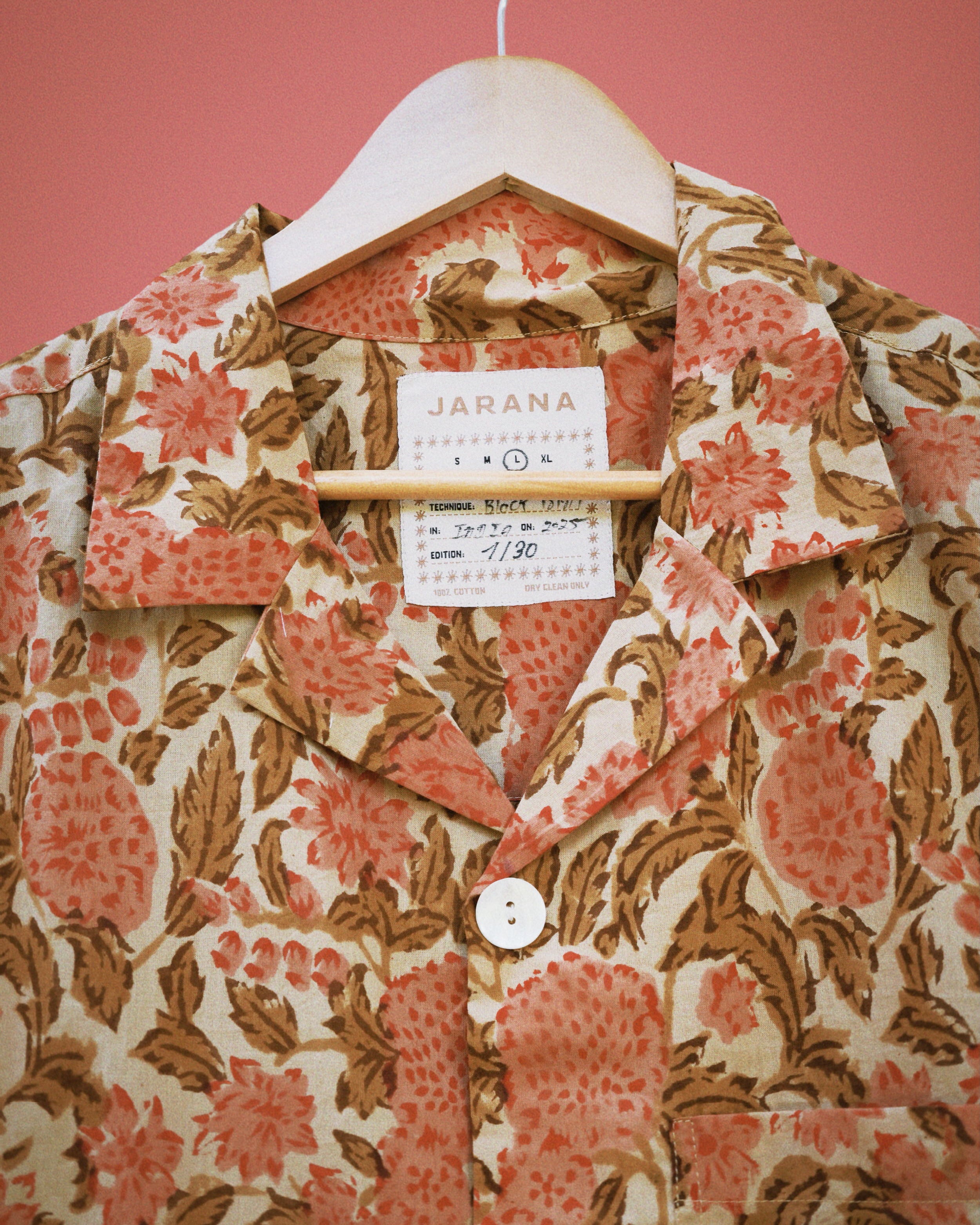 Soft coral floral block print on beige cotton shirt, showing resort collar and top shell button.