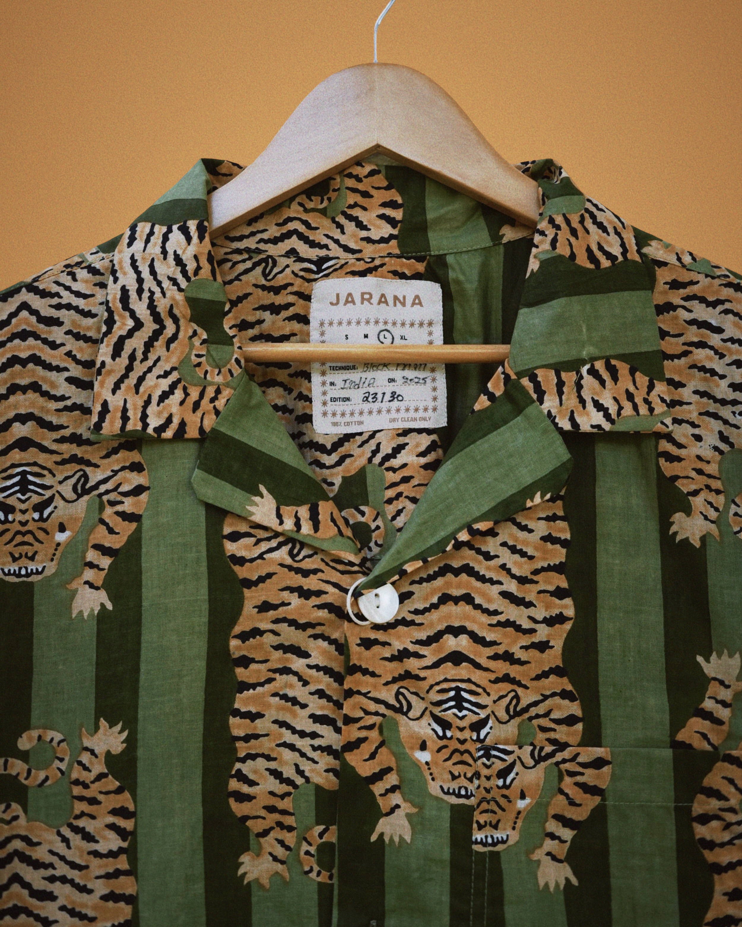Bold green striped shirt covered with mirrored tiger block print and pearly buttons on hanger.