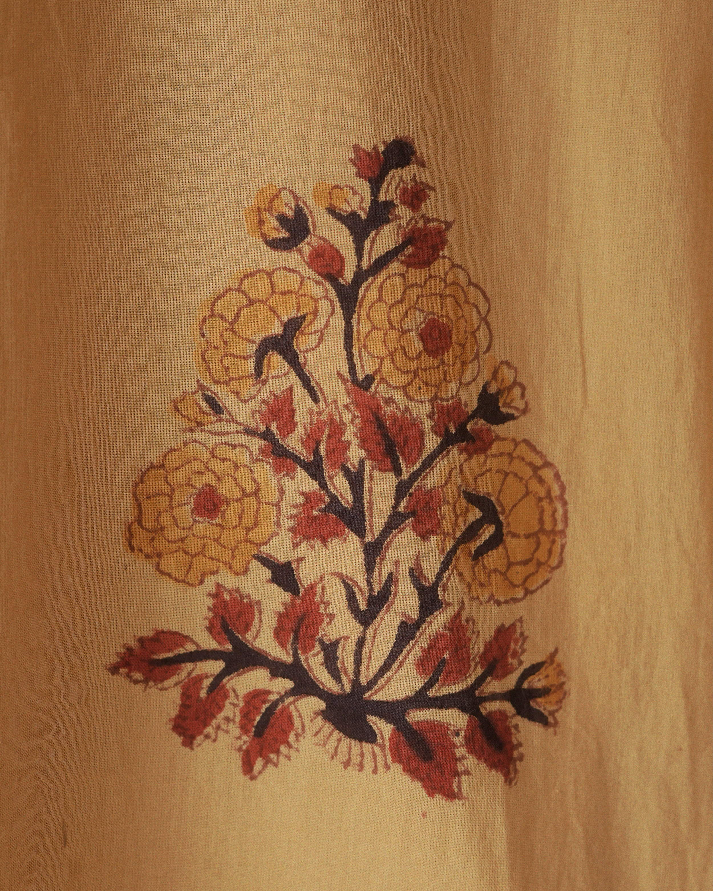 Detailed view of Jaranaβs yellow cotton shirt showing a hand-block-printed floral bouquet in red and gold tones.