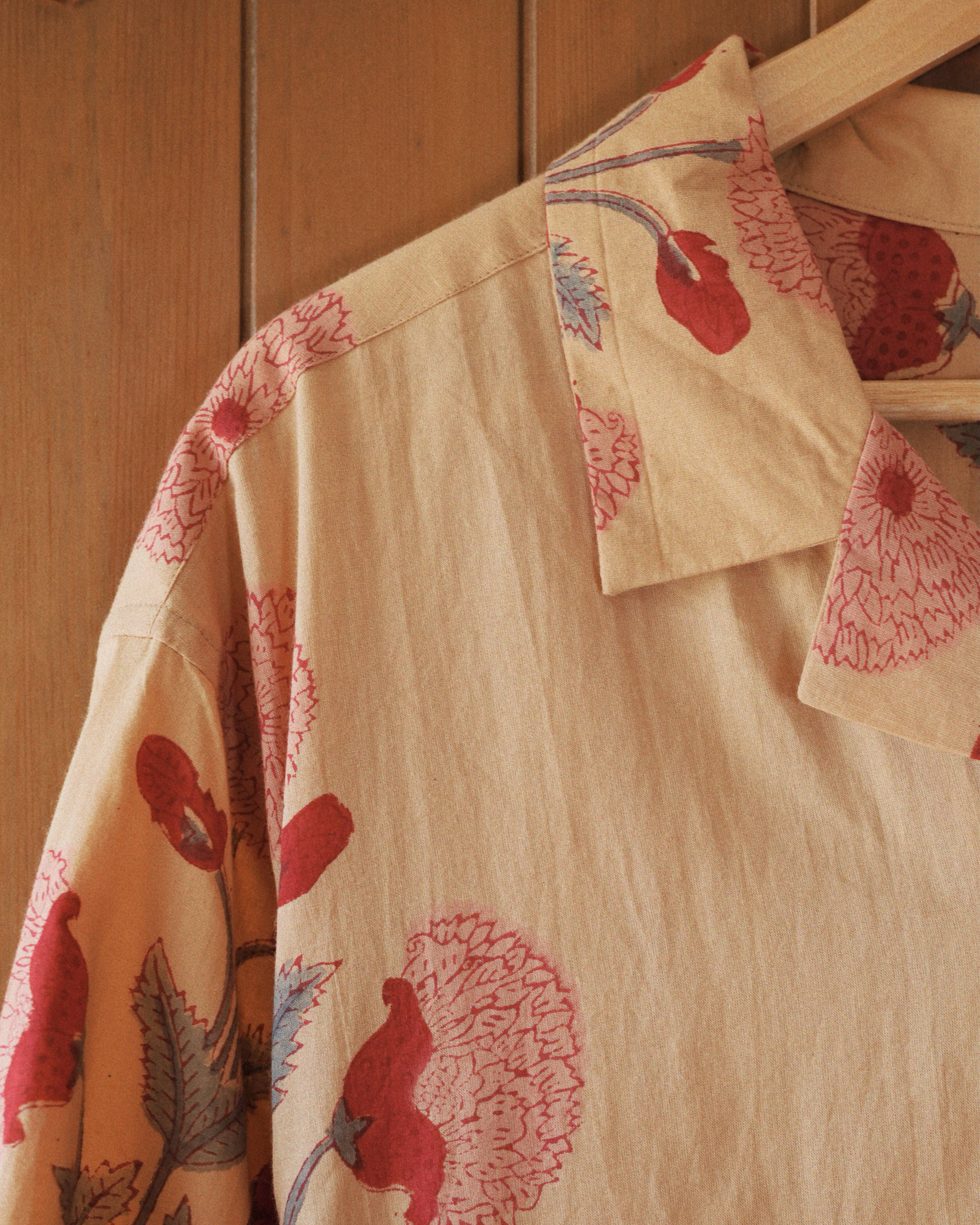 Shoulder and collar corner showing repeating red bud block print against light ochre fabric.