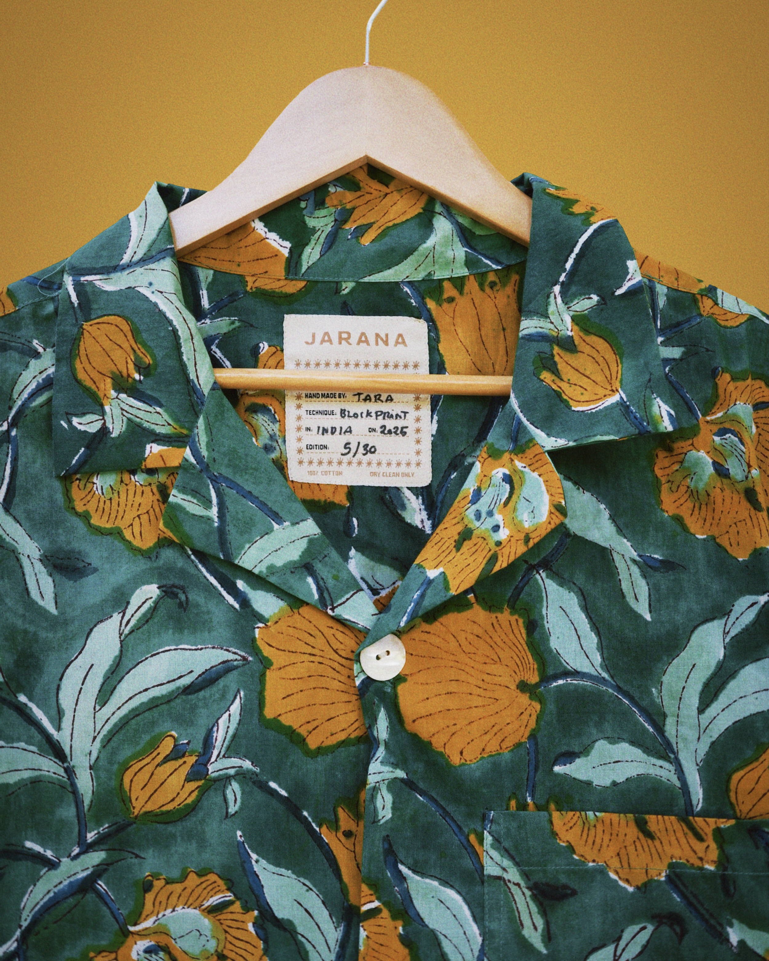 Detailed view of lush green cotton shirt featuring large gold flowers and leafy hand block print.