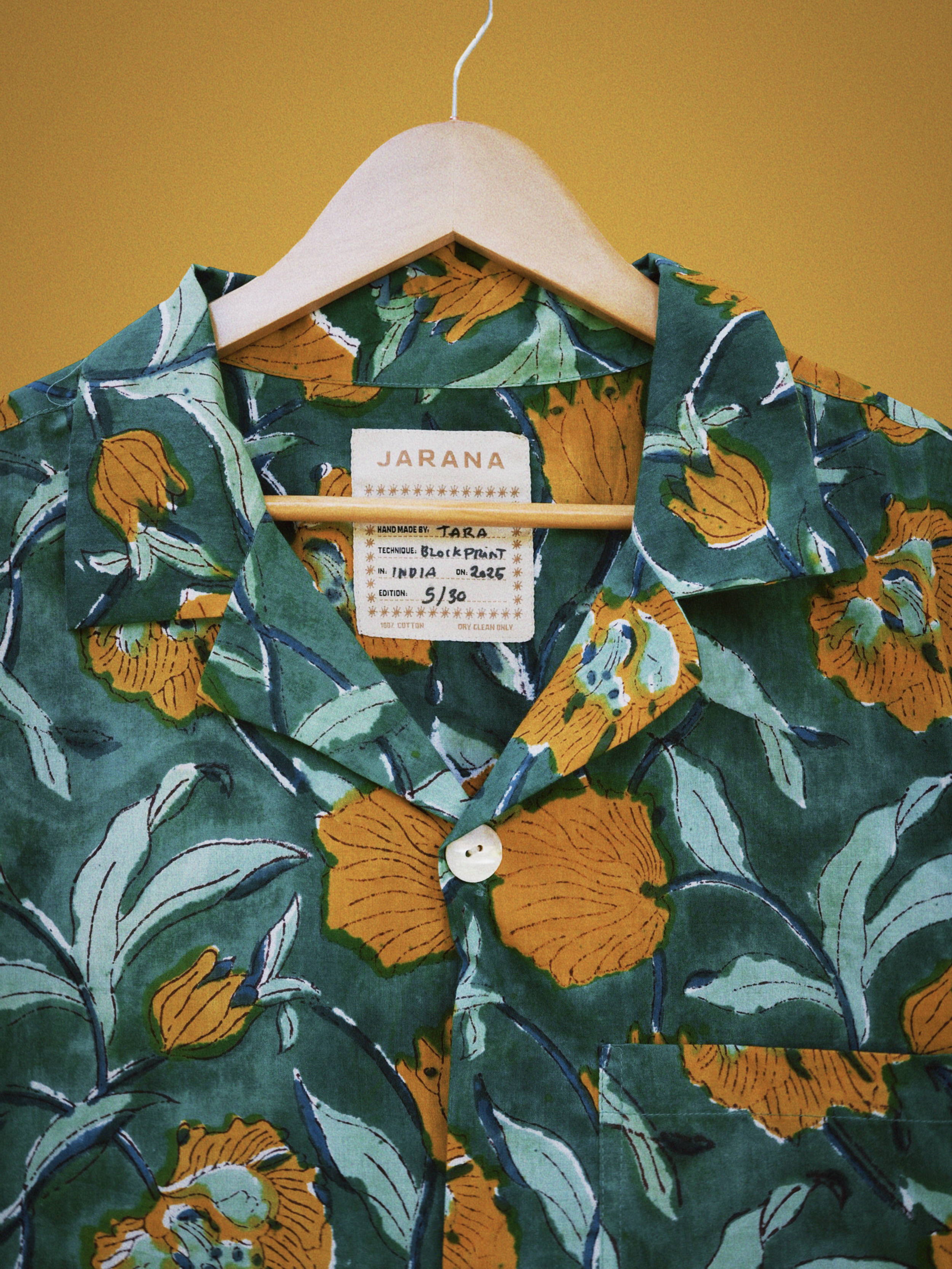 Detailed view of lush green cotton shirt featuring large gold flowers and leafy hand block print.