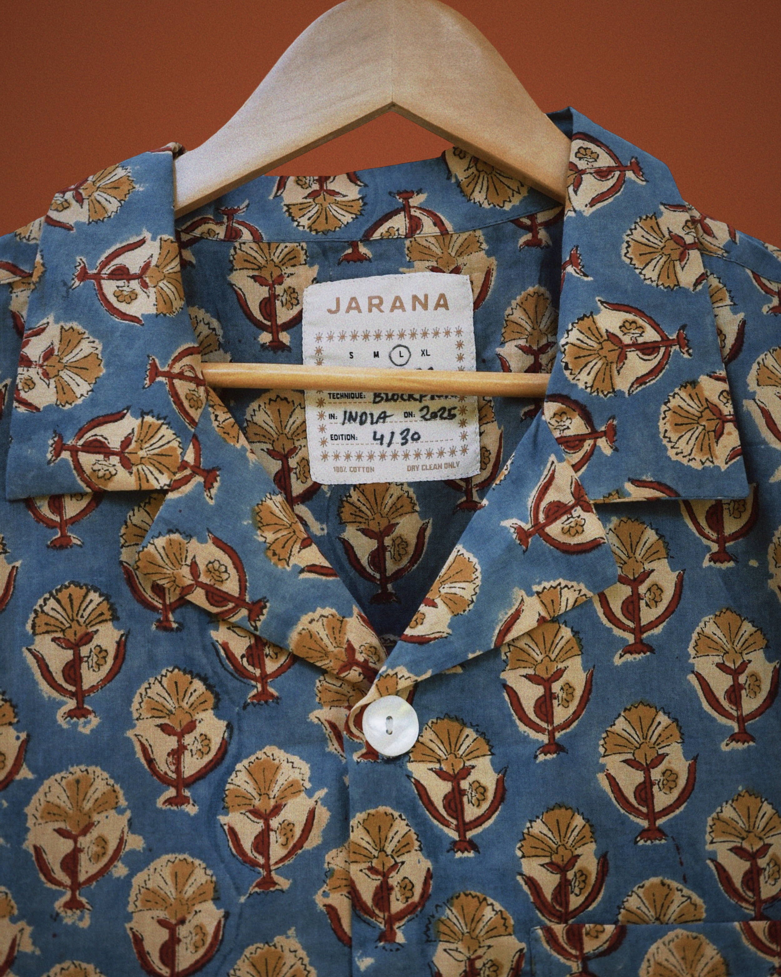 Blue indigo cotton shirt with repeating lotus emblem block print and white shell button detail.