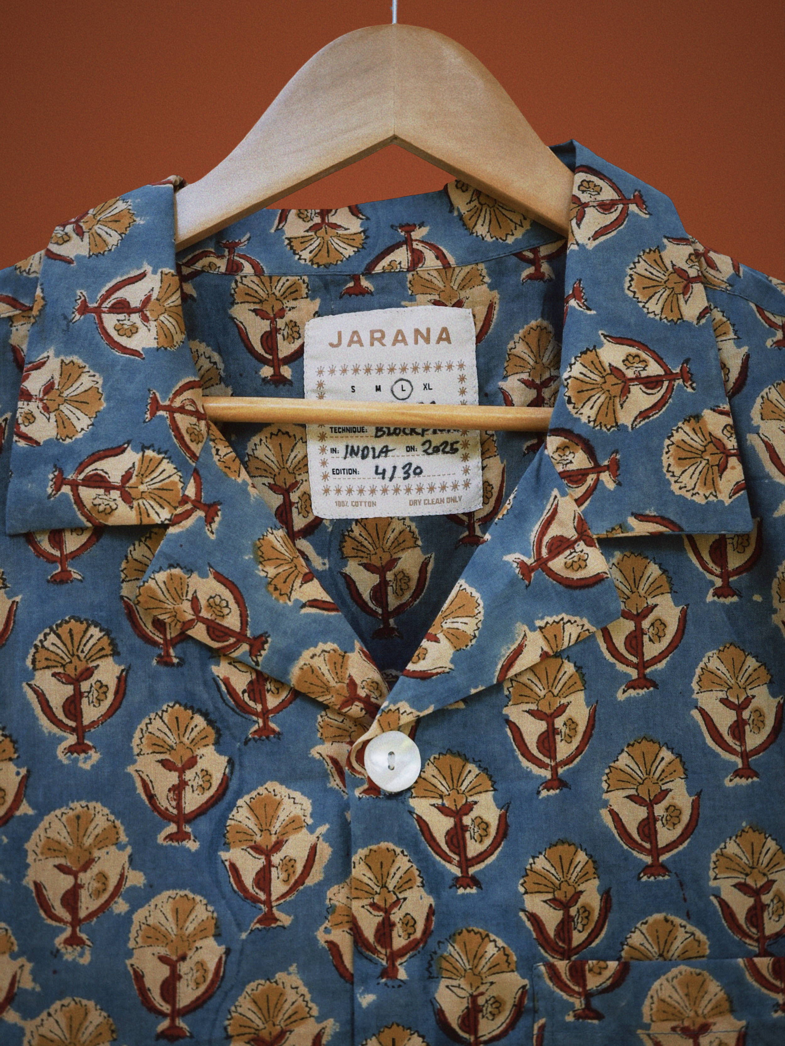 Blue indigo cotton shirt with repeating lotus emblem block print and white shell button detail.