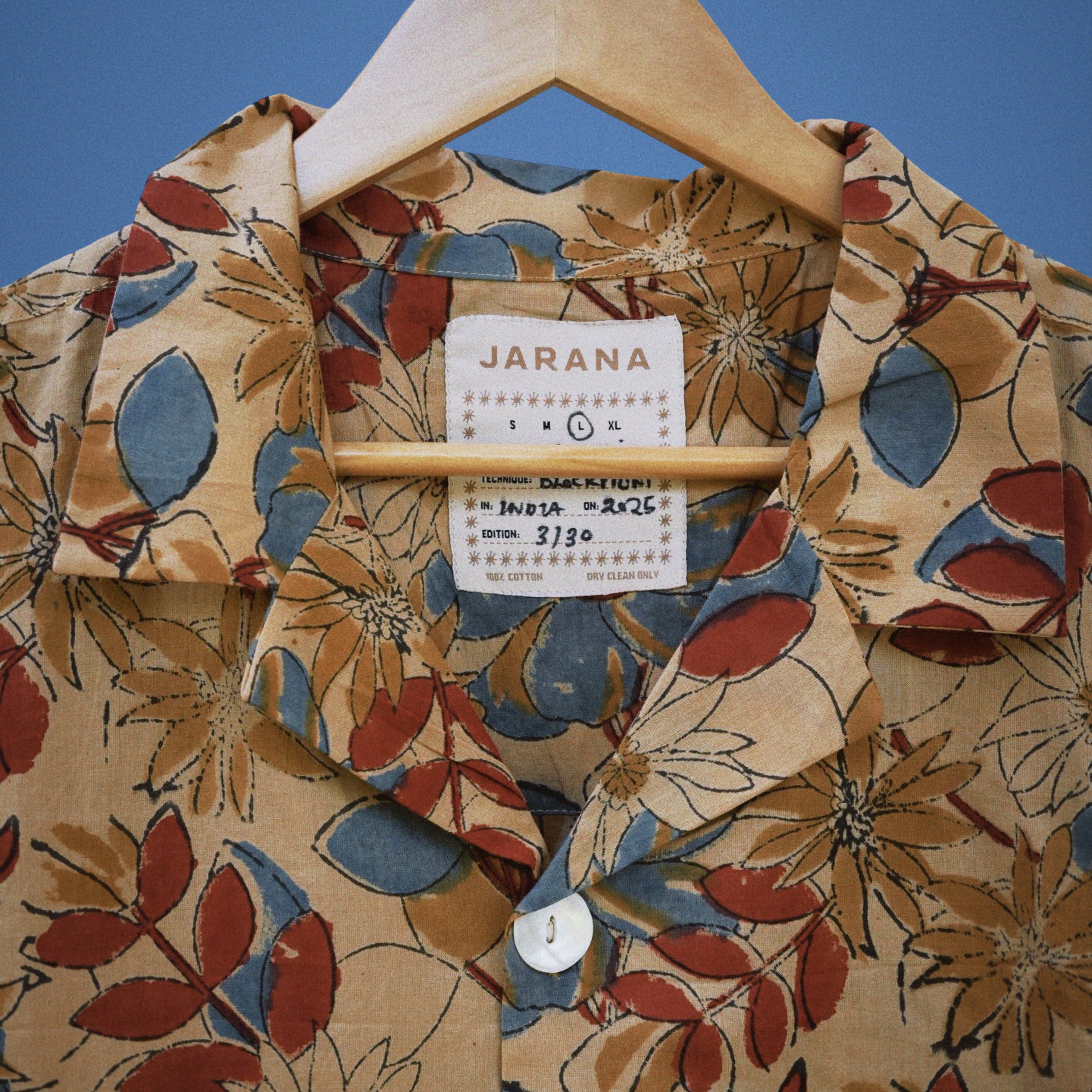 Ochre cotton shirt with red, blue, and tan hand-sketched floral pattern and single shell button.