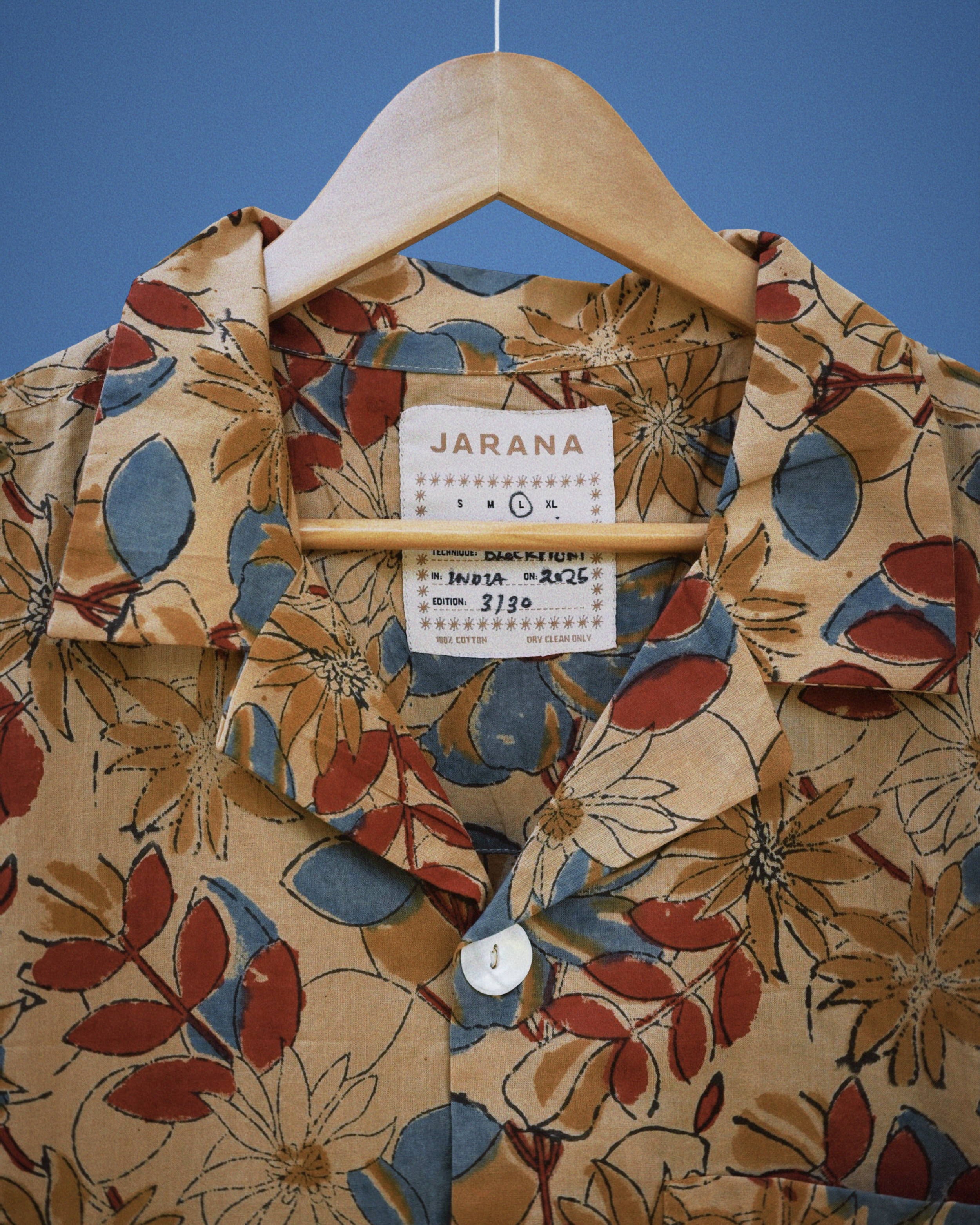 Ochre cotton shirt with red, blue, and tan hand-sketched floral pattern and single shell button.