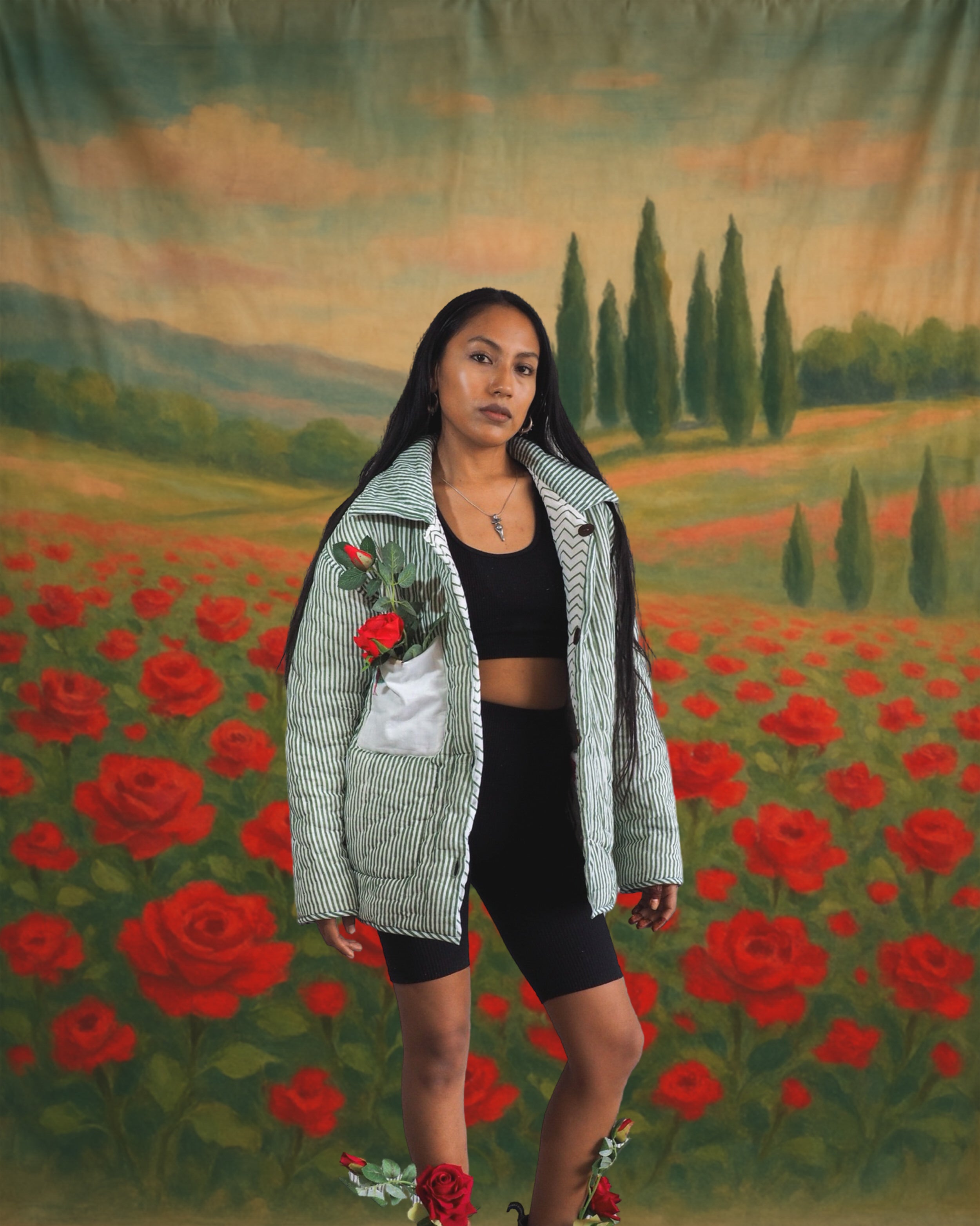 Model wearing handmade green-striped quilted jacket by Jarana, styled with red roses and set against a vintage rose field backdrop