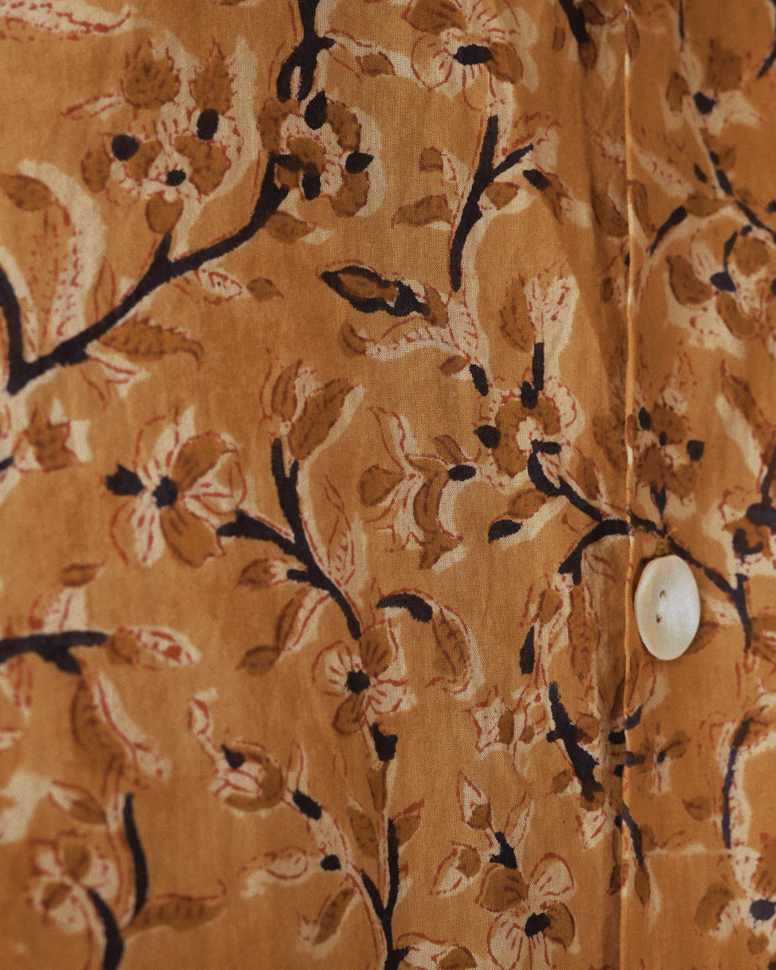 Macro view of Ramaje shirtβs sepia-toned floral block print with shell button and dark branch accents on soft cotton.