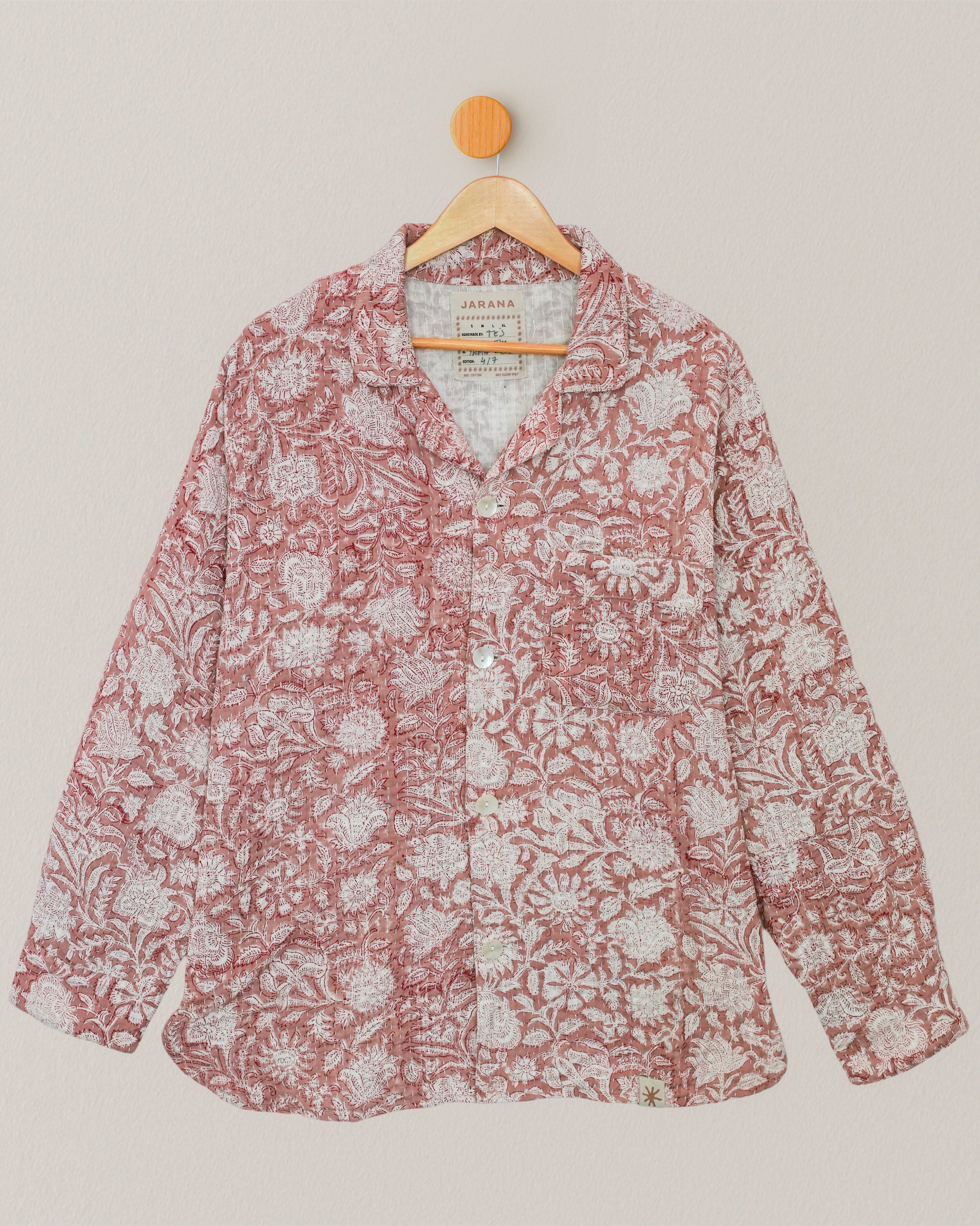 Full front view of a handcrafted Kantha shirt with red and white floral embroidery, hanging on wooden hanger