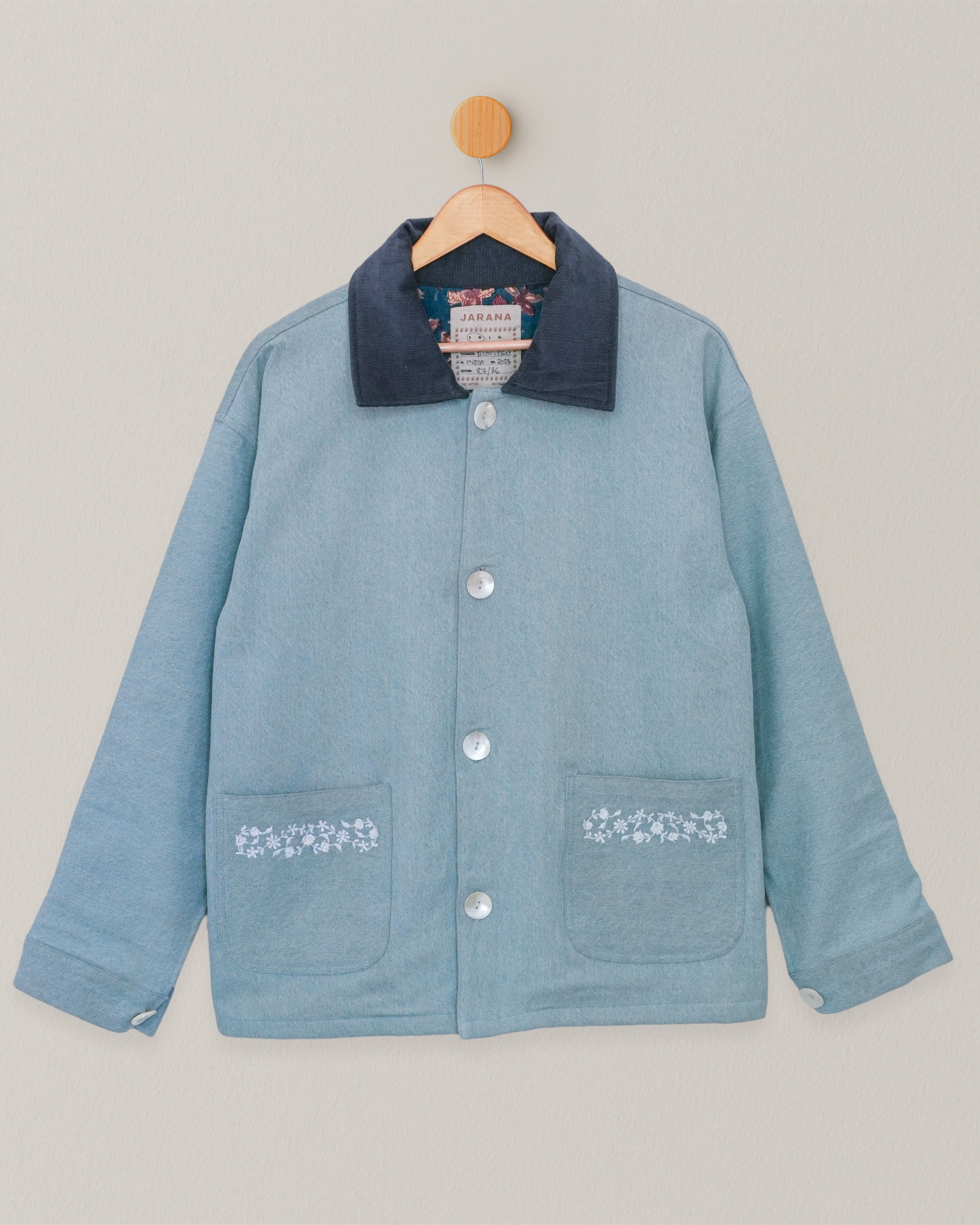 Front view of embroidered denim jacket with floral blockprint lining, hanging on wooden hanger