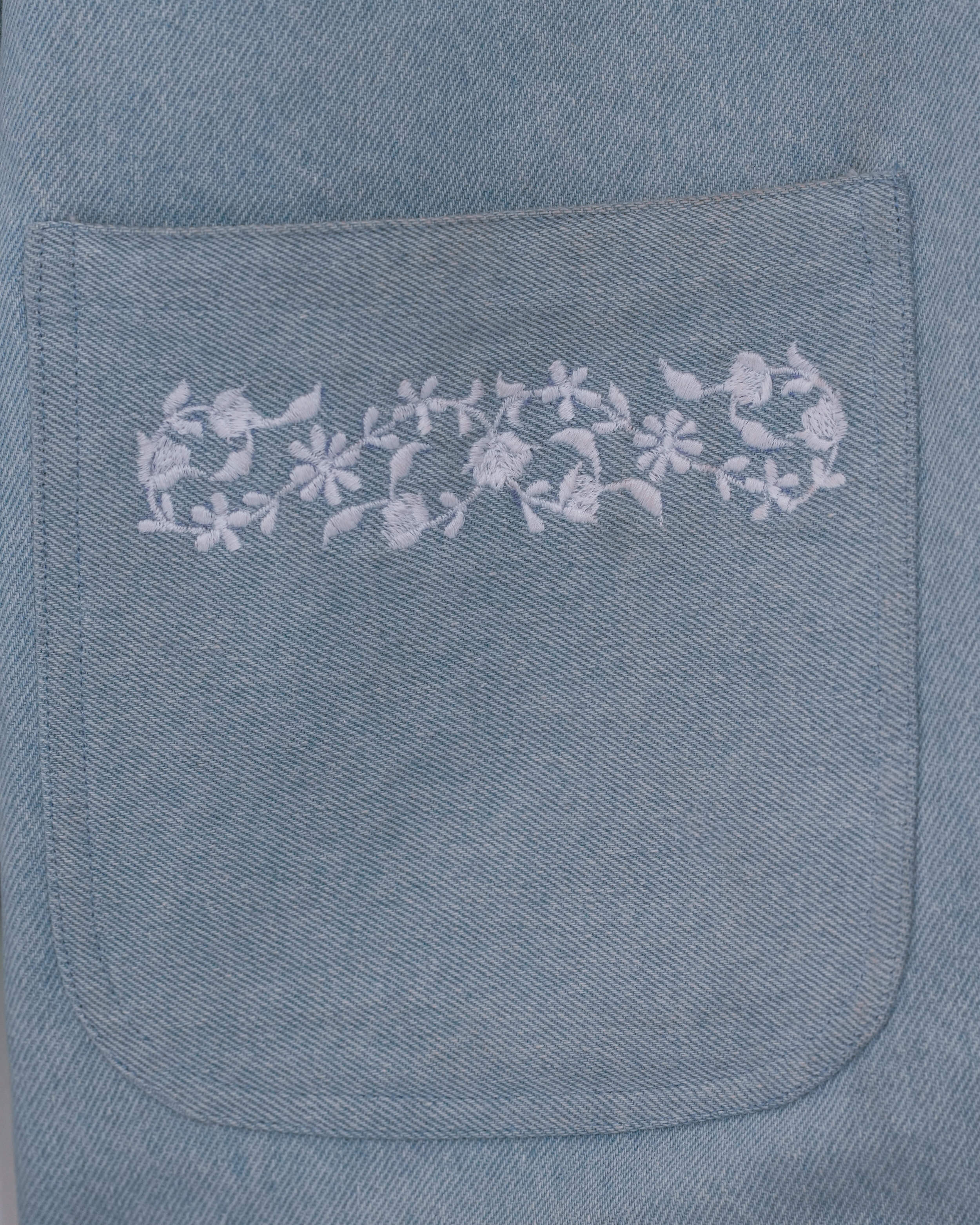 Close-up of white floral embroidery on jean-style front pocket of a light blue jacket