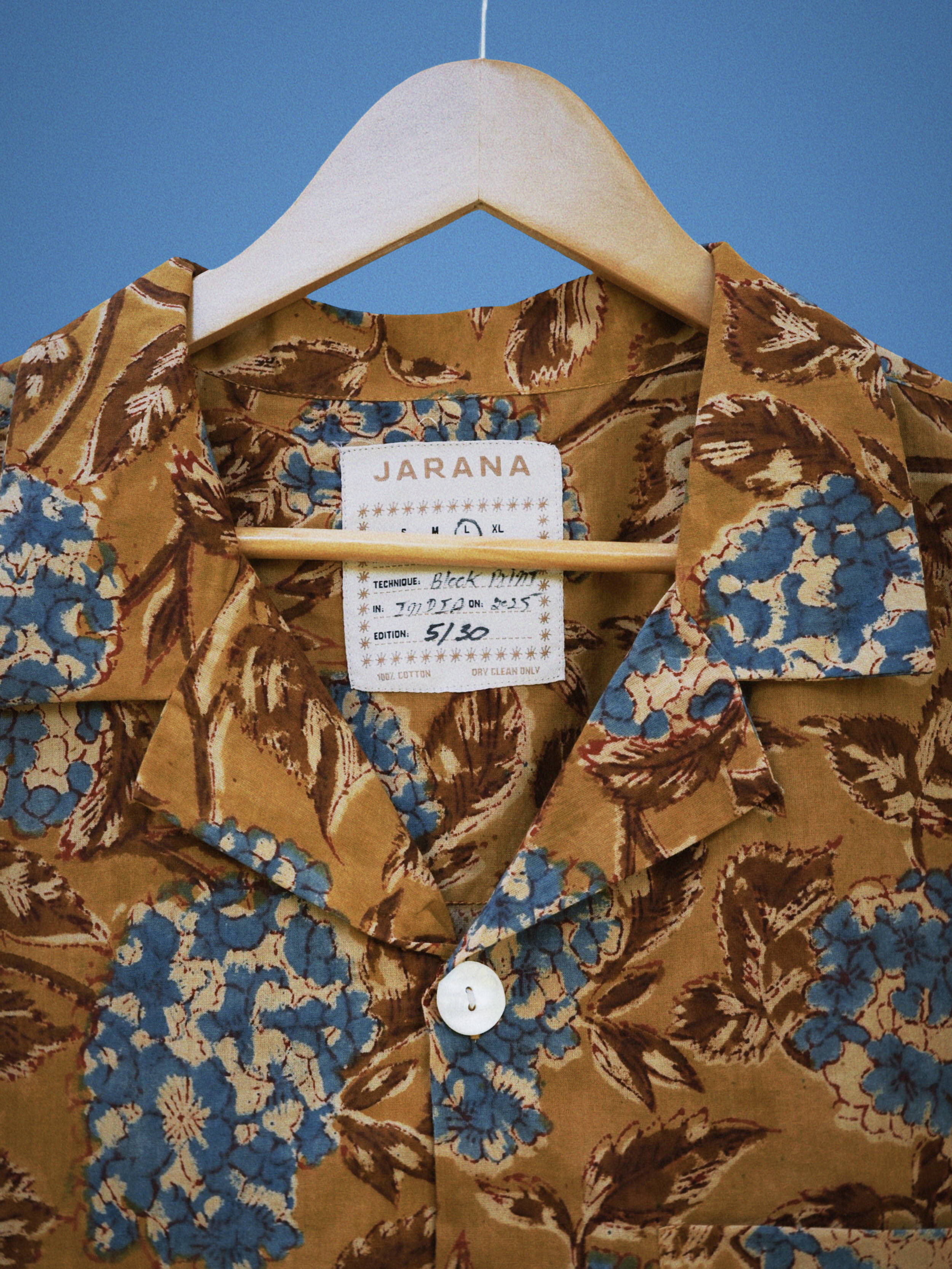 Close view of blue hydrangea and brown leaf block print on retro-toned cotton shirt with white button.
