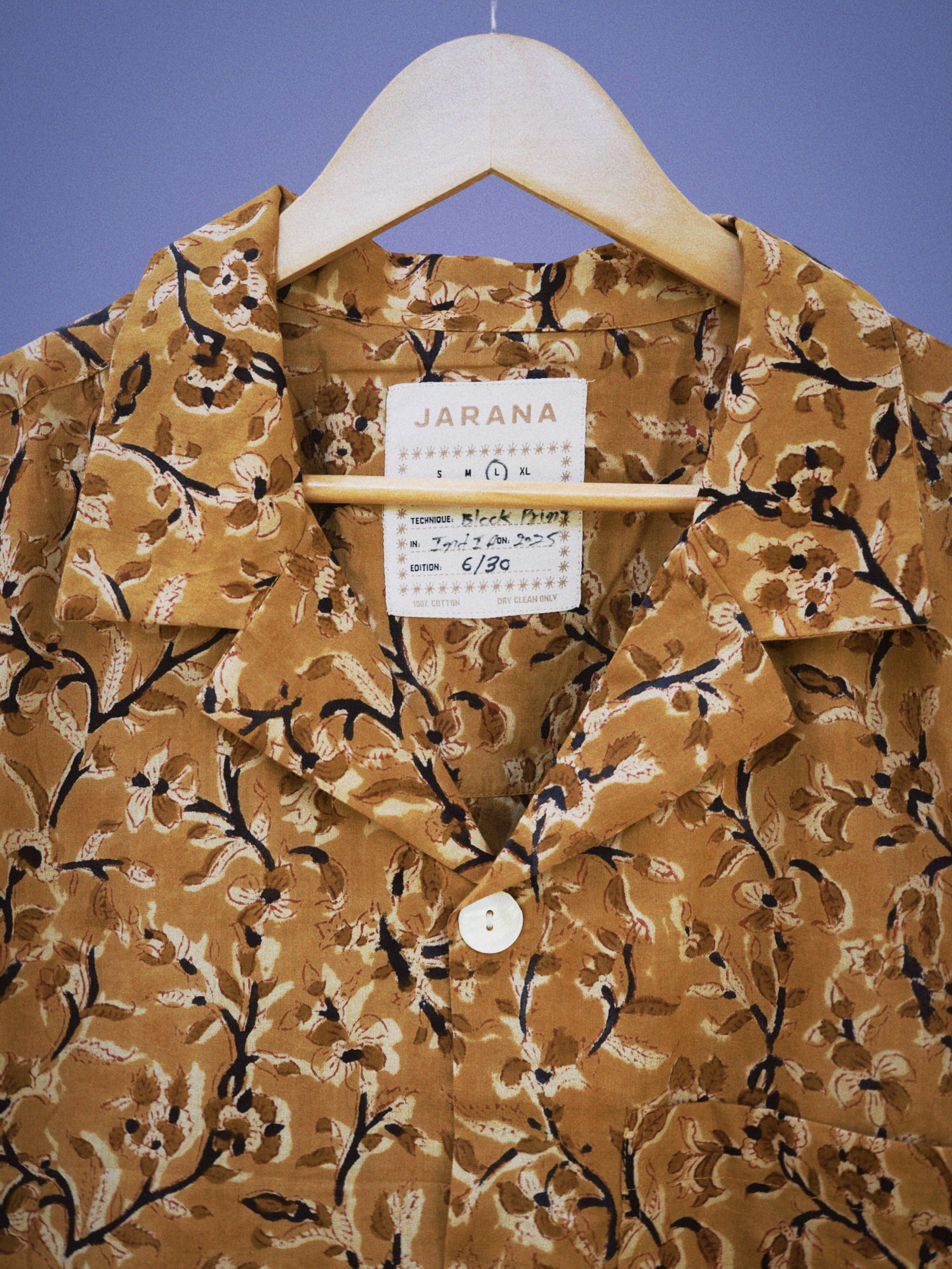 Close-up of brown cotton shirt with fine sepia floral block print and shell button, hanging on hanger.