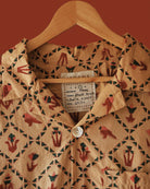 Detailed view of Carioca shirt’s resort collar and Jarana label, showing red parrot and green diamond block-print motifs on sandy cotton.