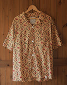 Full front view of Carioca short-sleeve cotton shirt featuring all-over red parrot and green geometric block print, hanging on wooden door.