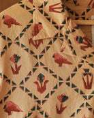 Close-up of hand block-printed pattern with red parrots, green triangles, and abstract flowers on beige cotton fabric.