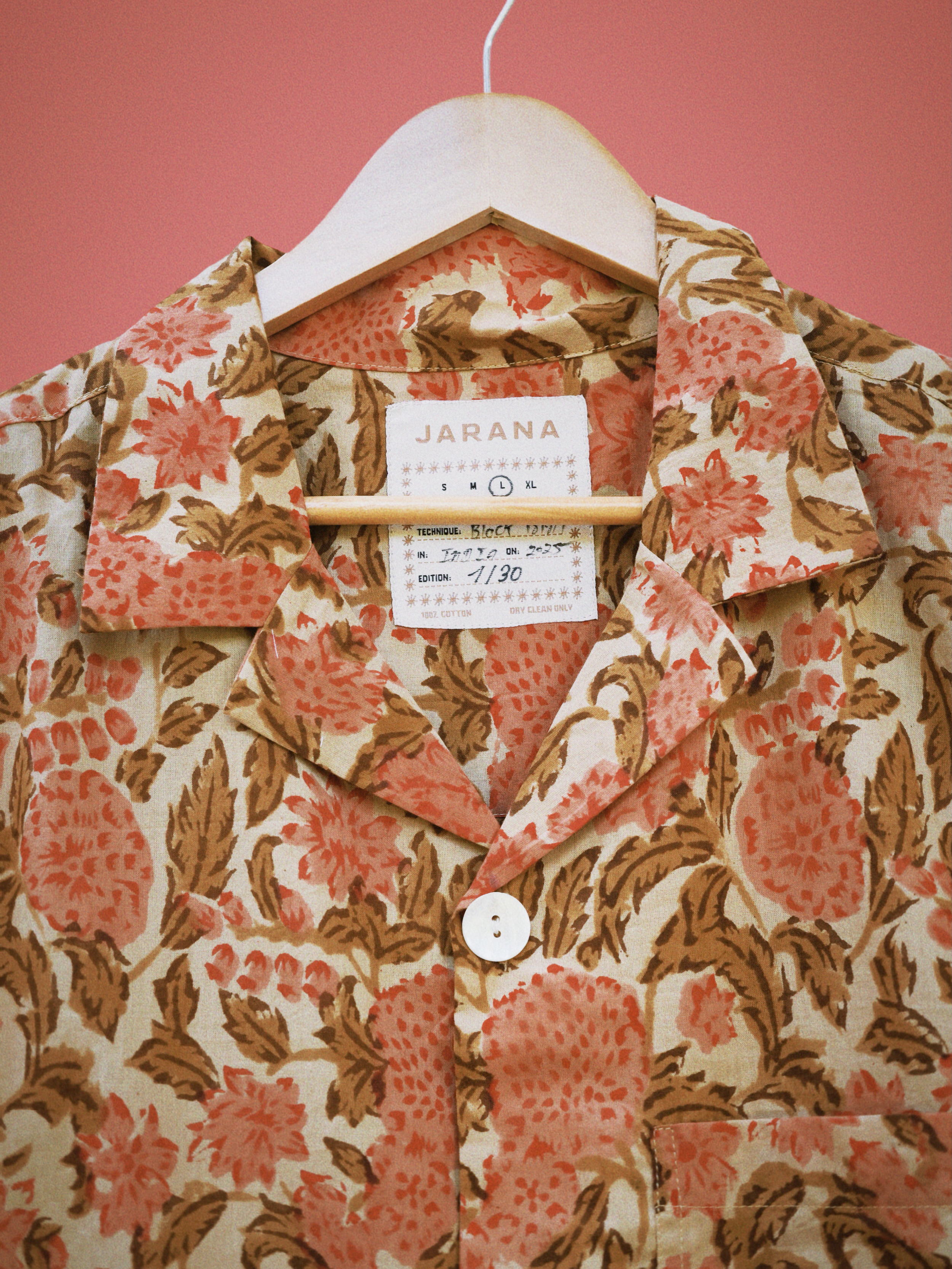 Soft coral floral block print on beige cotton shirt, showing resort collar and top shell button.