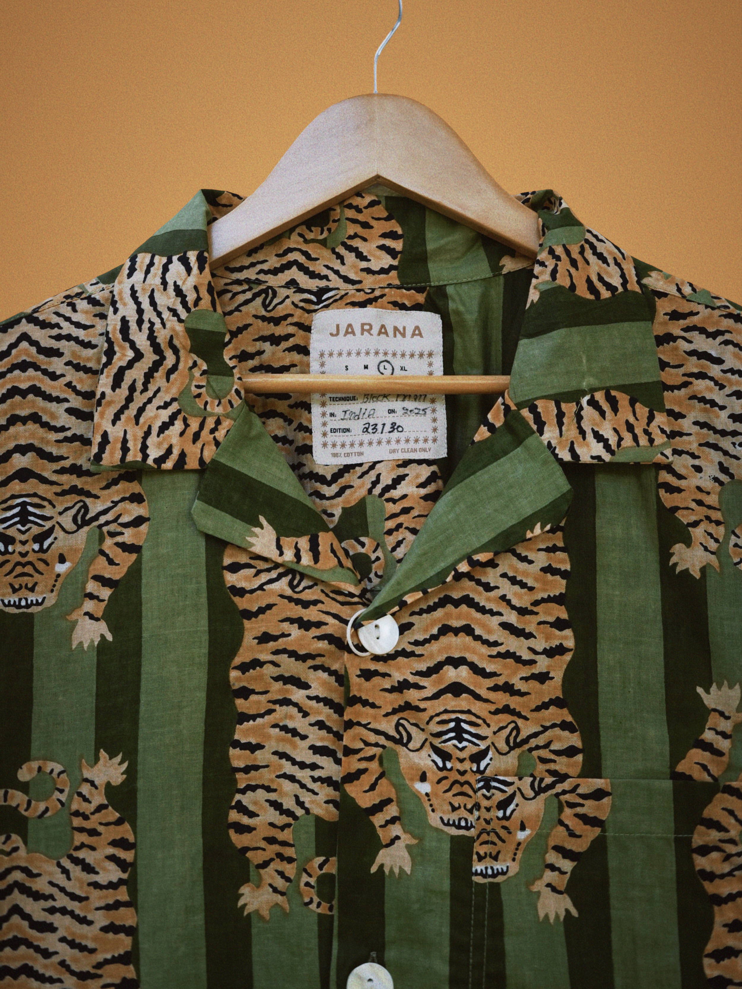 Bold green striped shirt covered with mirrored tiger block print and pearly buttons on hanger.