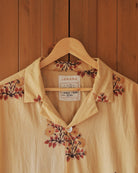Upper section of the Flor Baja shirt highlighting the open resort collar, shell button, and floral print near the placket.