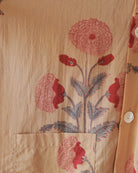 Angled view of side pocket and shell button highlighting red buds and blue-green leaves on soft yellow cotton.