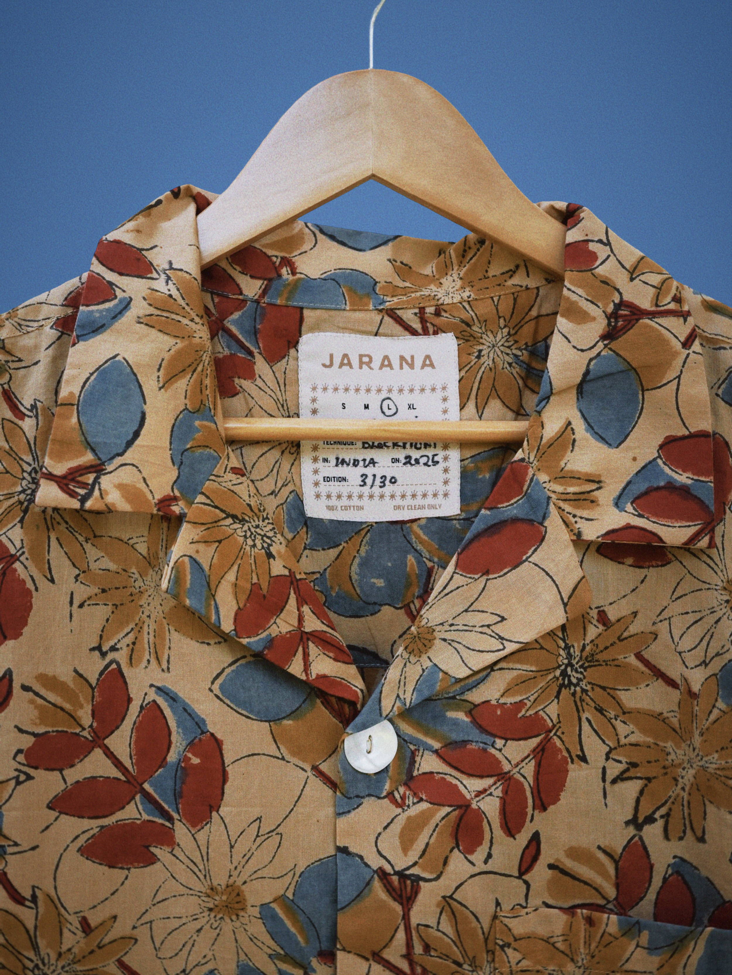 Ochre cotton shirt with red, blue, and tan hand-sketched floral pattern and single shell button.