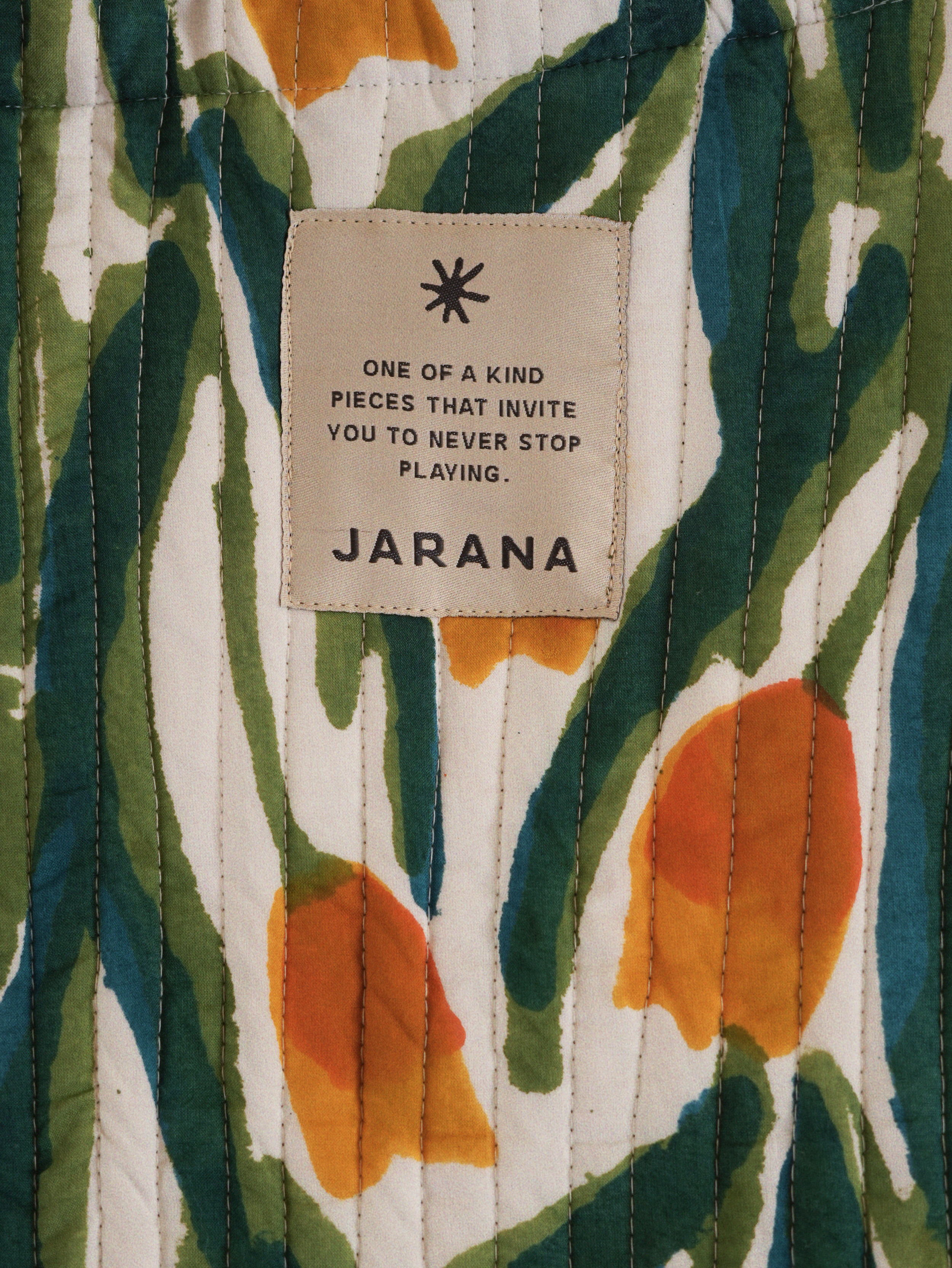 Detail of quilted cotton showing painterly green stems and orange buds alongside the Jarana label.