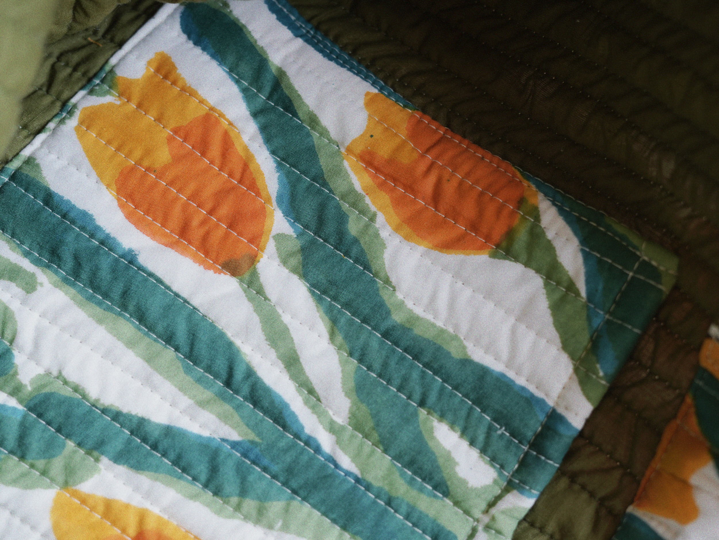 Interior detail of quilted tote with hand-printed orange buds and flowing green stems on soft cotton.