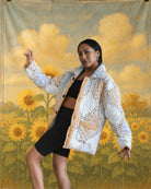 Model wearing white quilted jacket with blue and beige Kashmiri-style embroidery by Jarana, posing in front of a painted sunflower backdrop.