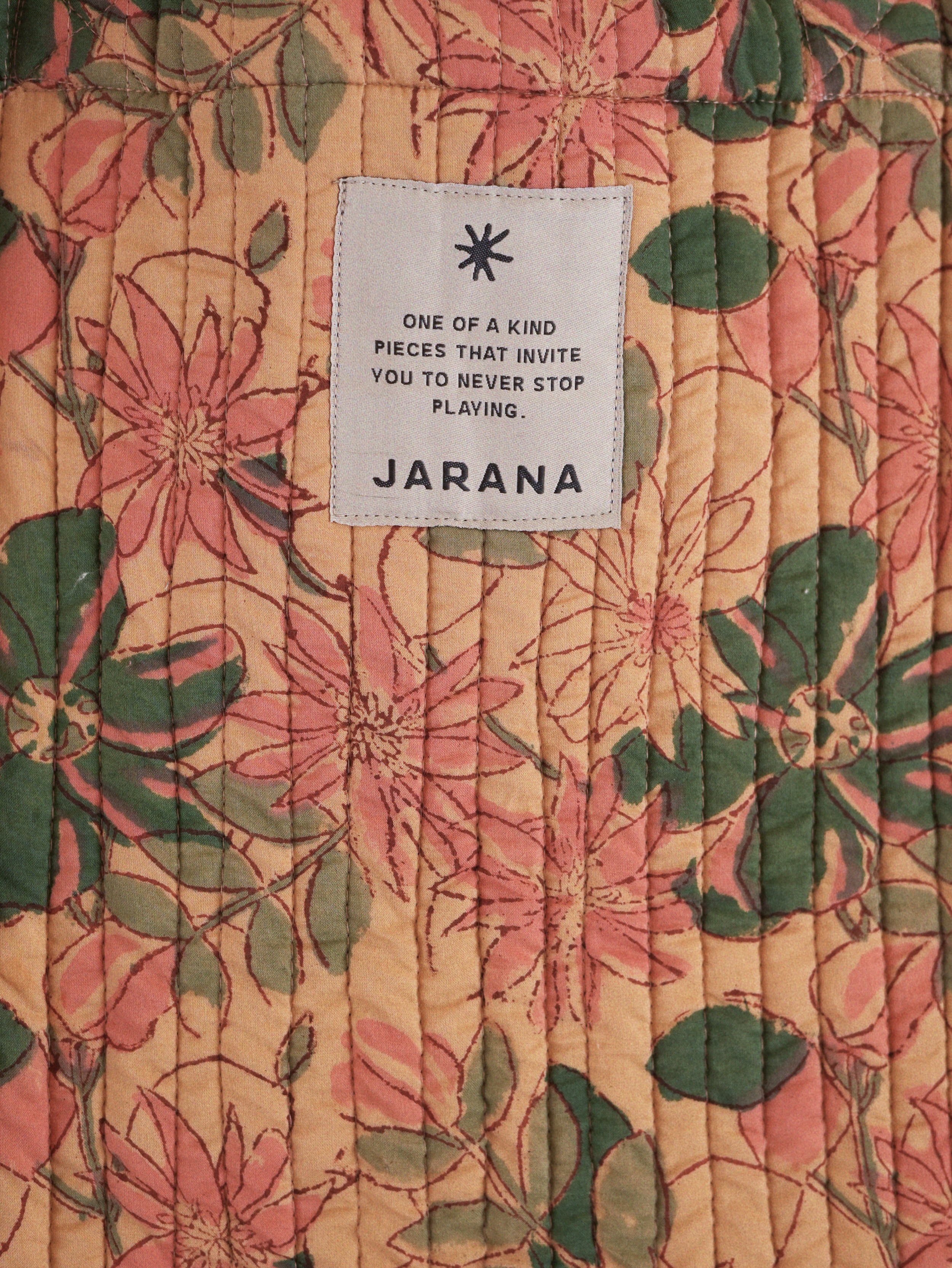 Peach-toned quilted fabric featuring pink and green floral block print with a stitched Jarana label.