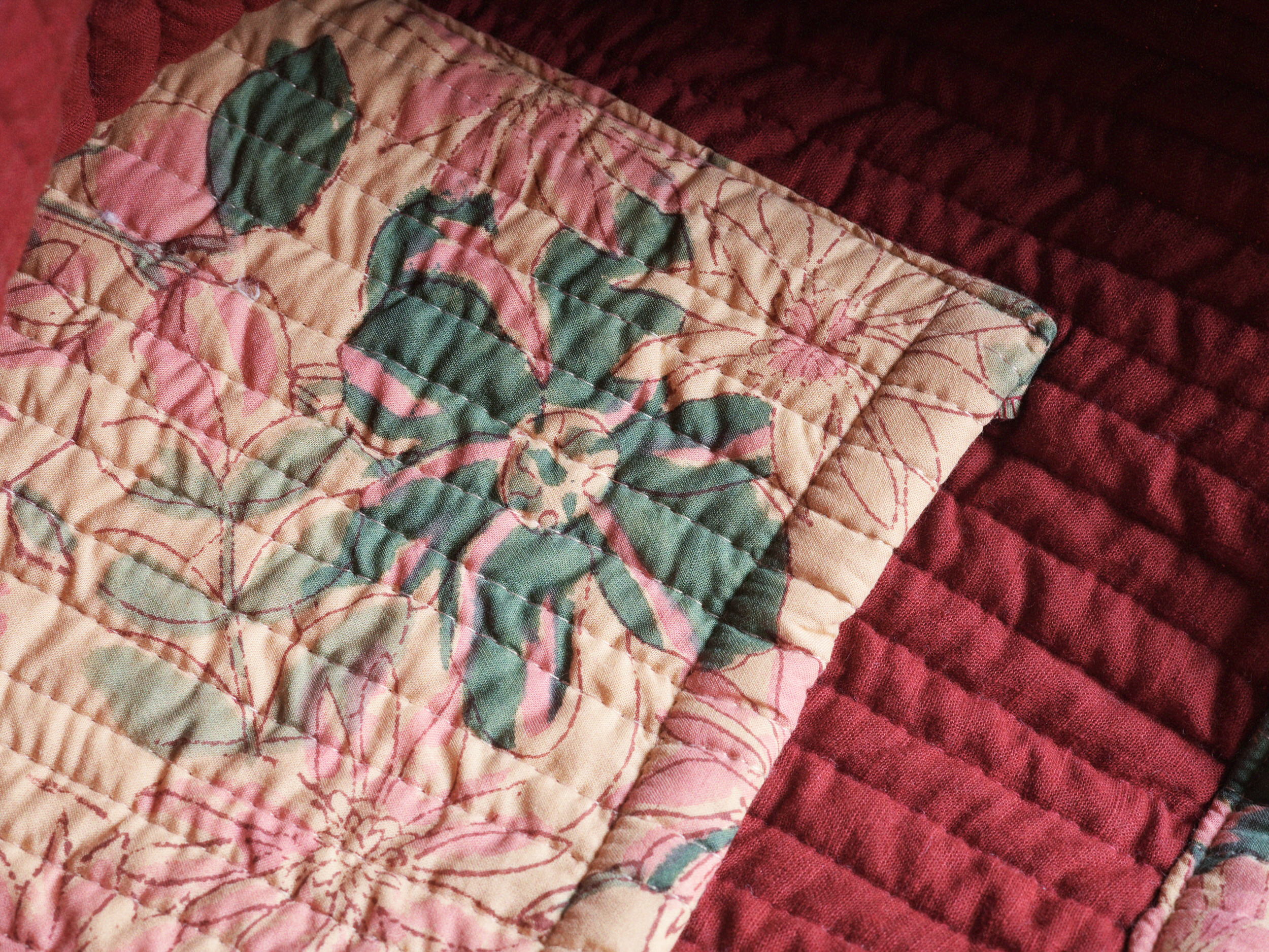 Patchwork panel of muted pink and green floral print set against a deep ruby quilted lining.