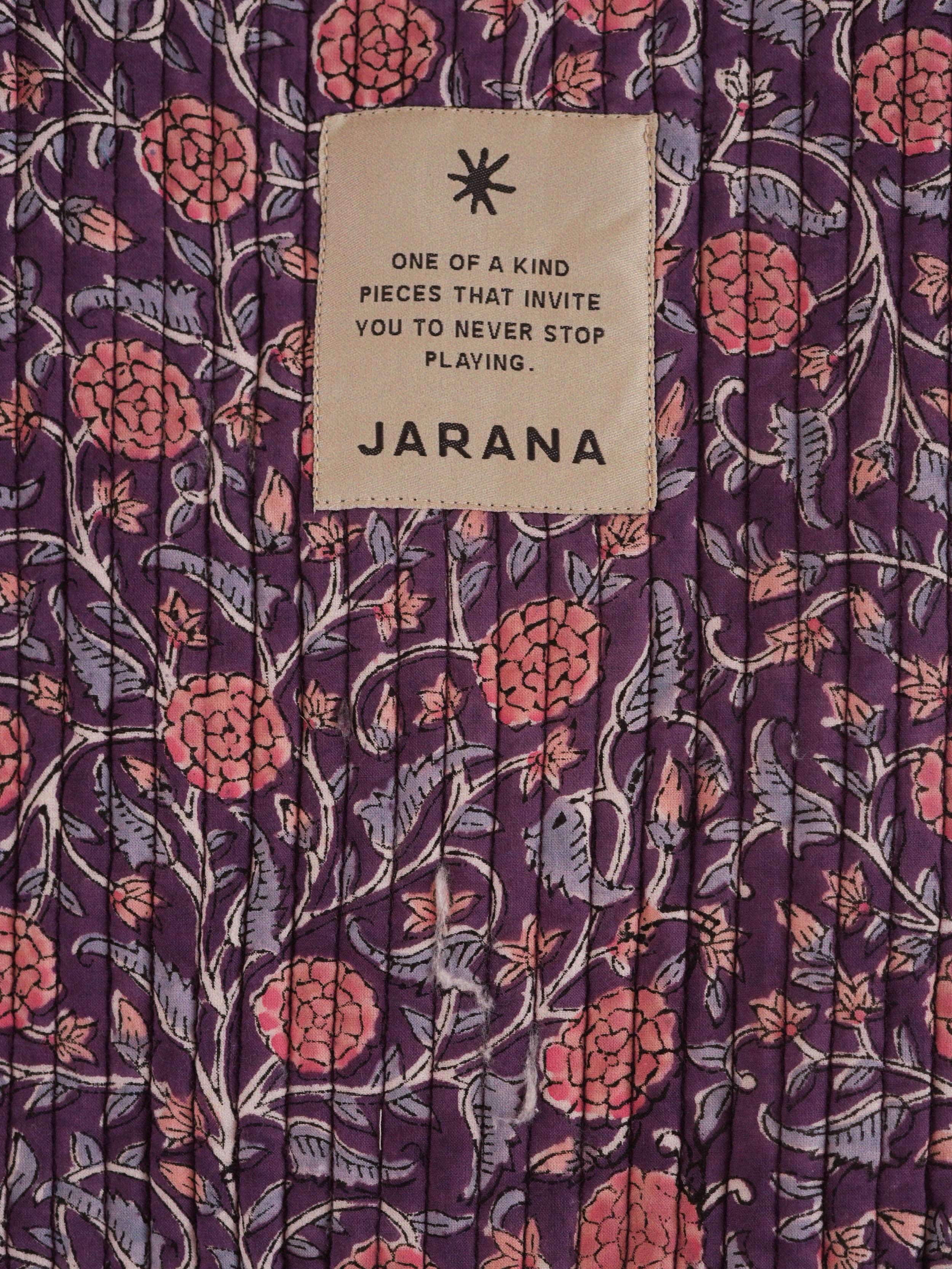 Close-up of purple quilted cotton covered in pink floral block print, accented by a Jarana badge.