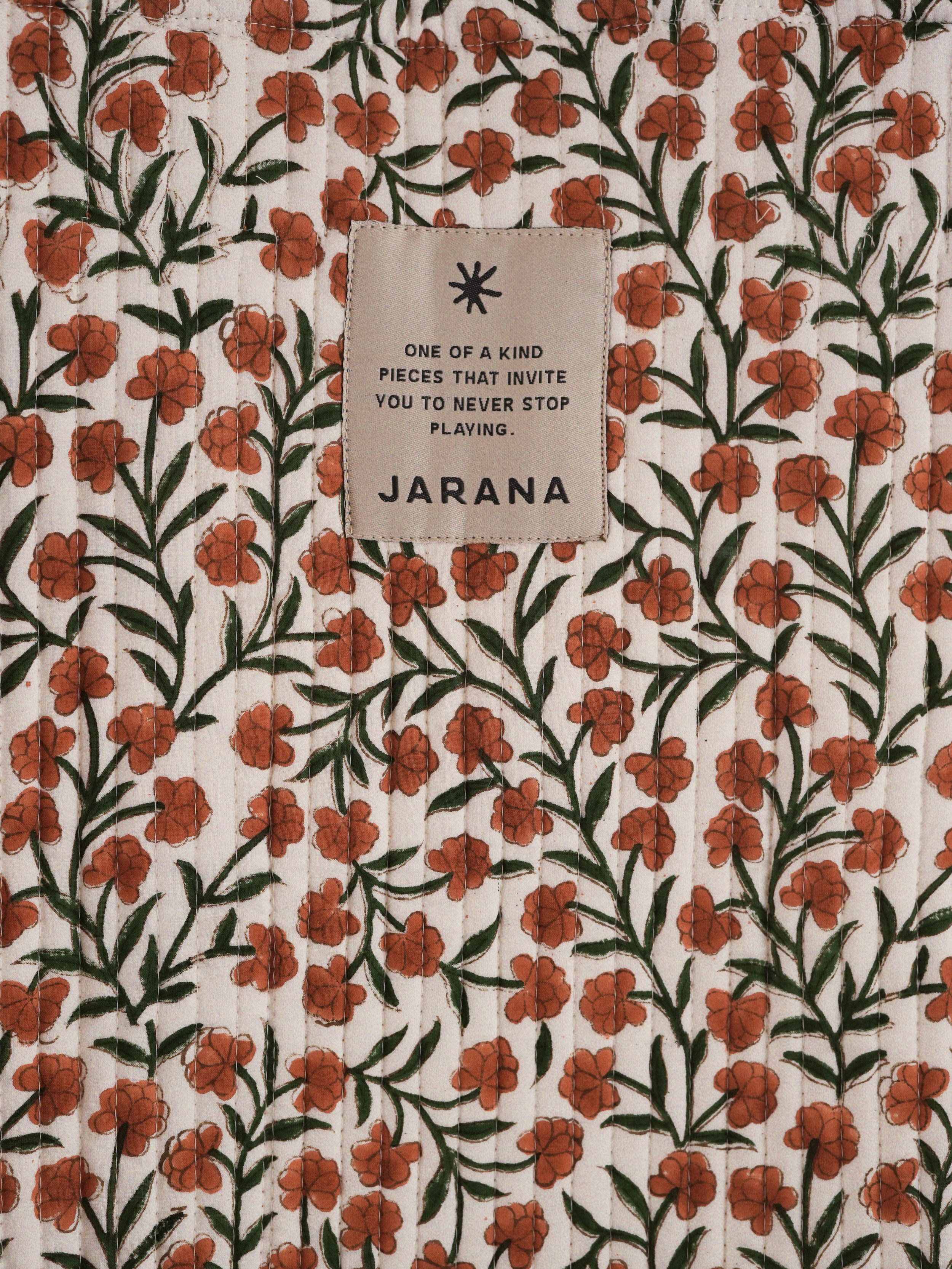 Quilted cotton fabric densely printed with small orange flowers and a centered Jarana brand tag.