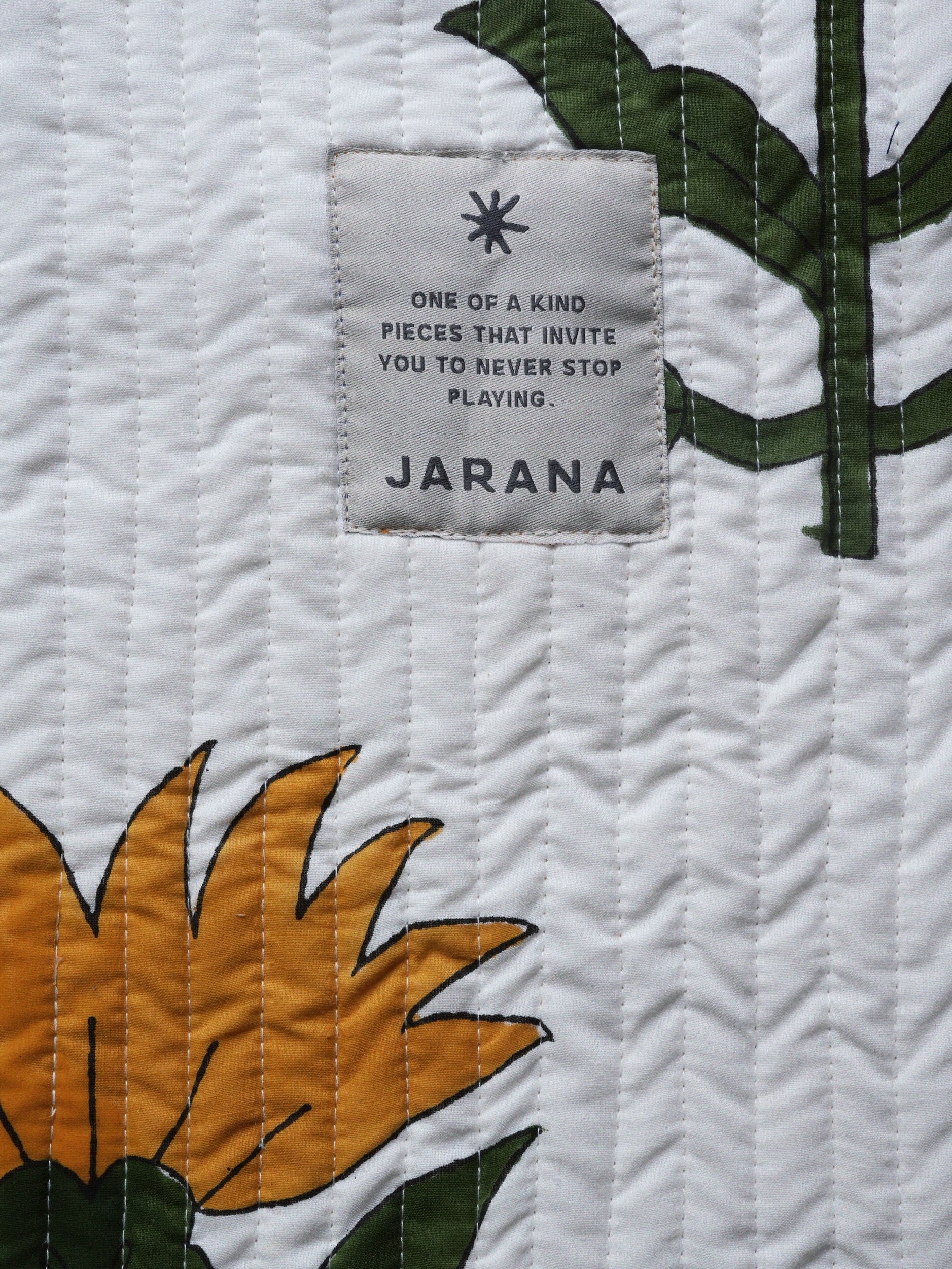 Close-up of quilted white cotton showing oversized sunflower block print and the stitched Jarana label.