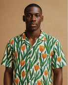 Studio portrait of male model wearing Jarana short-sleeve shirt covered in orange tulip block print with green stems on natural cotton.