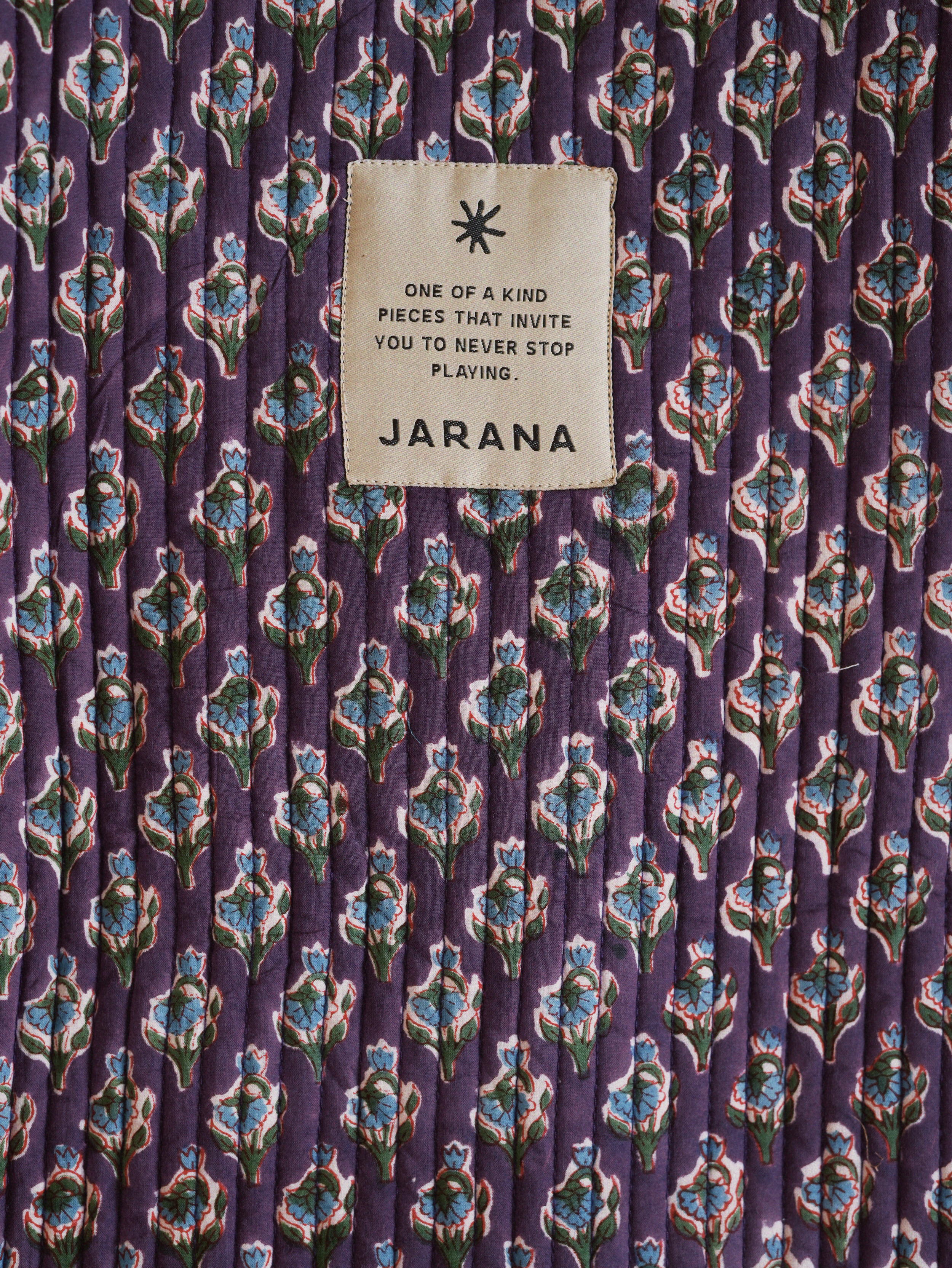 Close-up of Jarana violet quilted tote bag showing block print floral design and stitched brand label with playful motto.