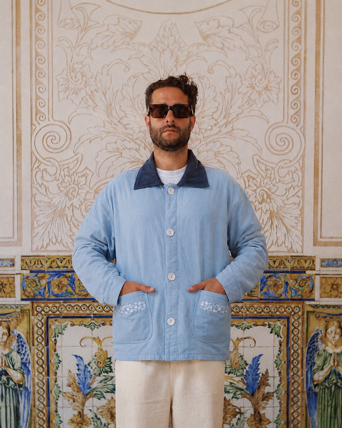Man wearing a light blue jacket with a patterned wall in the background