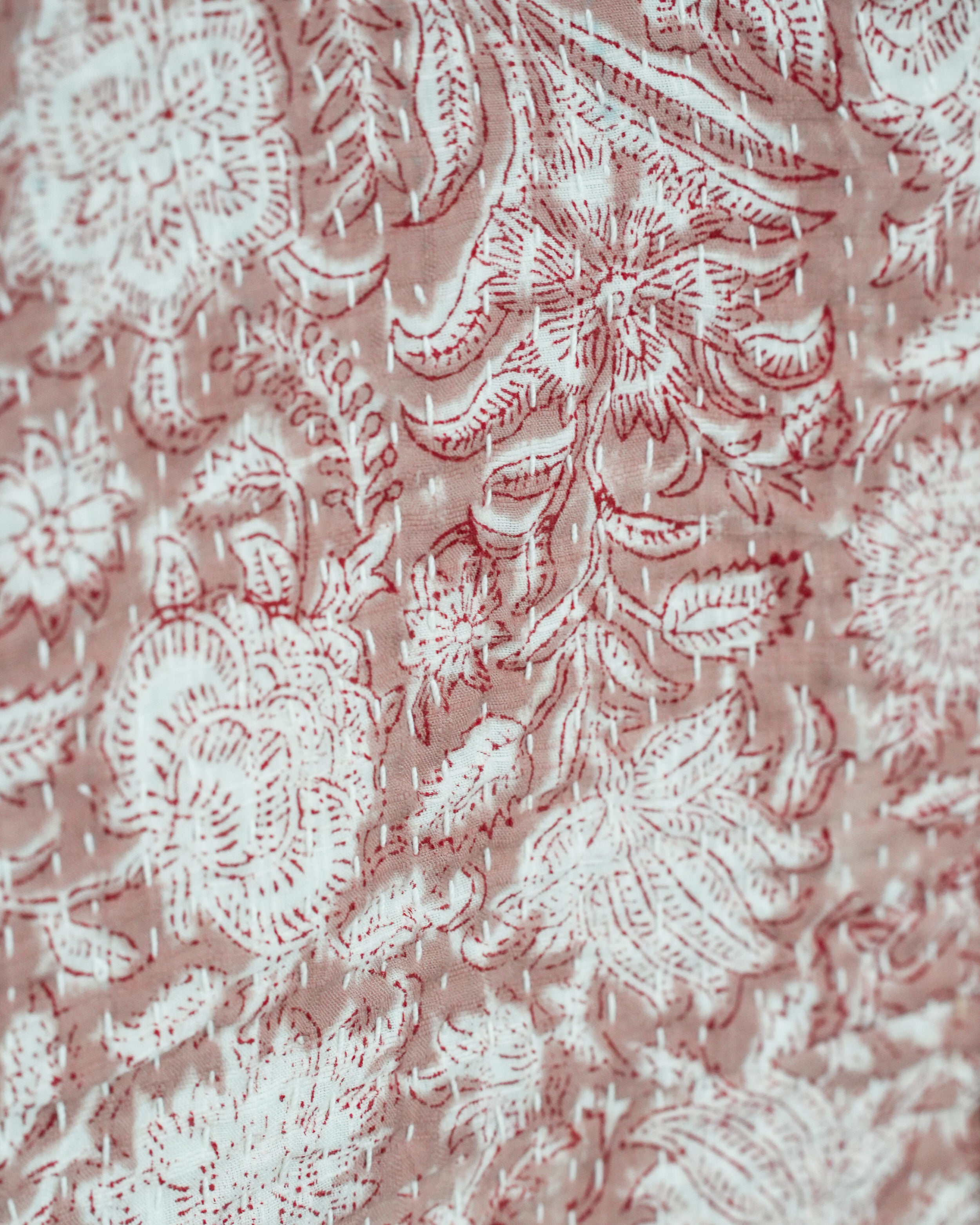 Close-up of hand-stitched Kantha embroidery in red and white floral pattern on soft cotton fabric