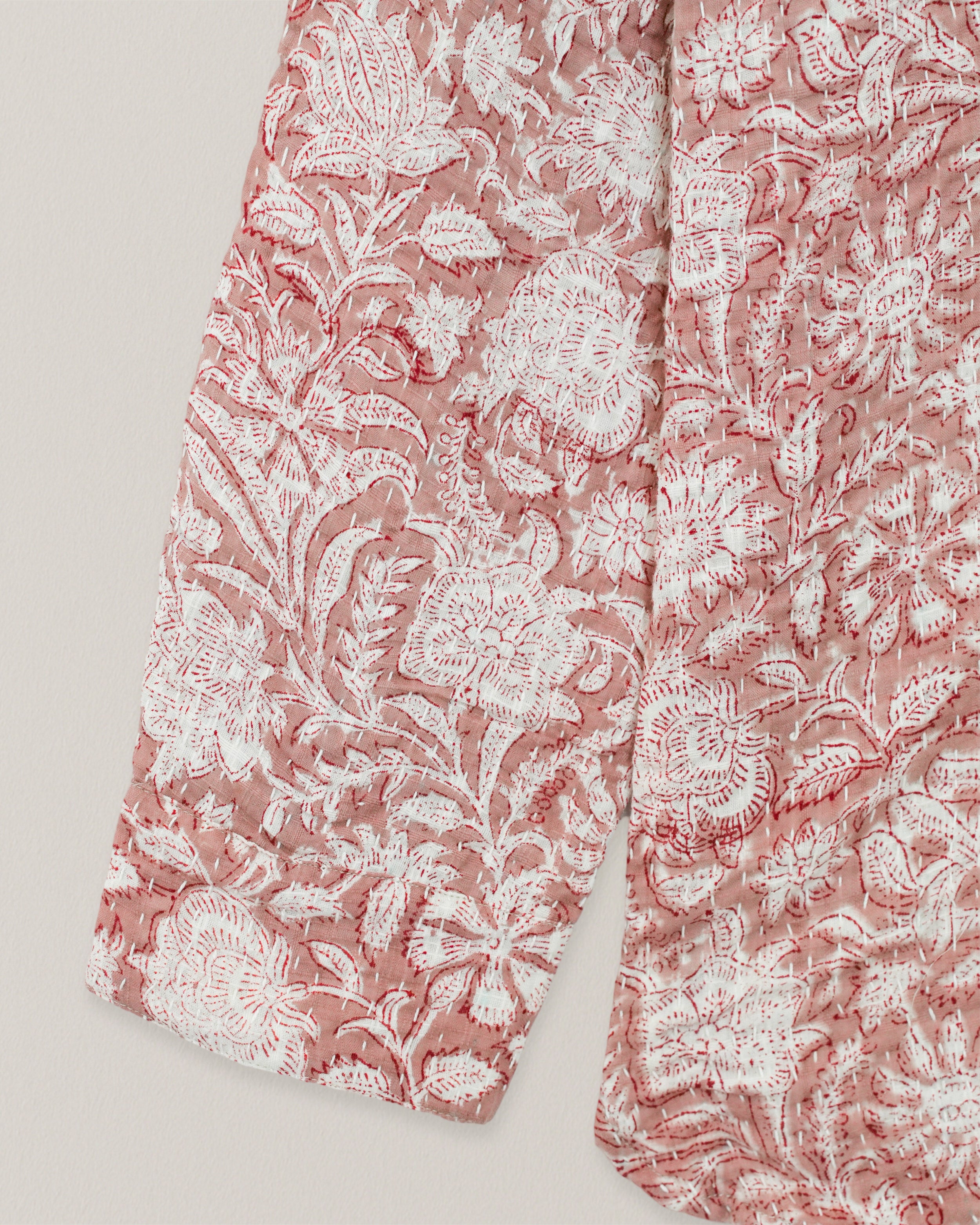 Close-up of shirt sleeve and hem with traditional floral Kantha embroidery on red cotton fabric
