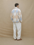 Person wearing a patterned jacket and white pants against a beige background