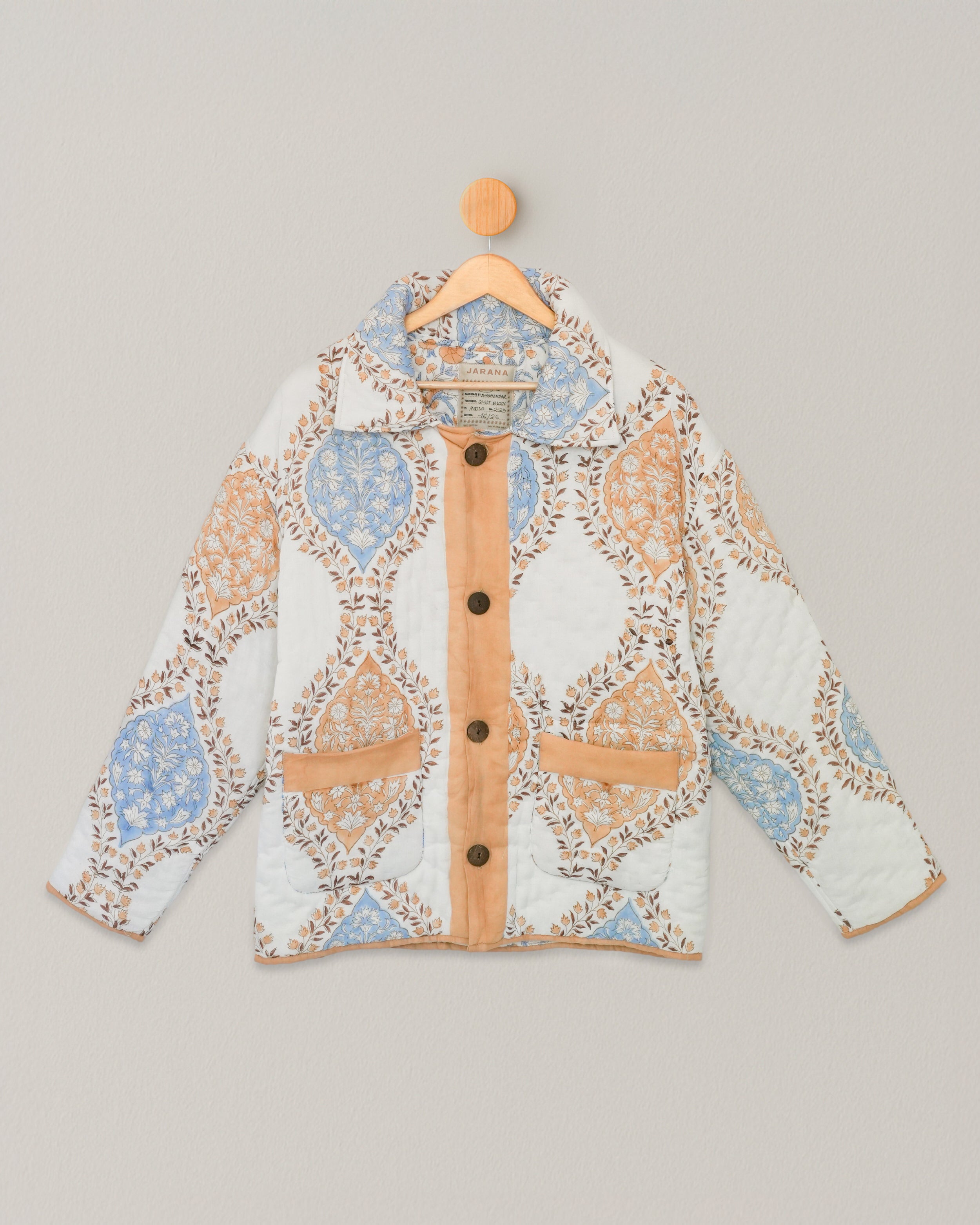 Front view of quilted cotton jacket with tan piping and blue-orange floral blockprint, hanging on wooden hanger