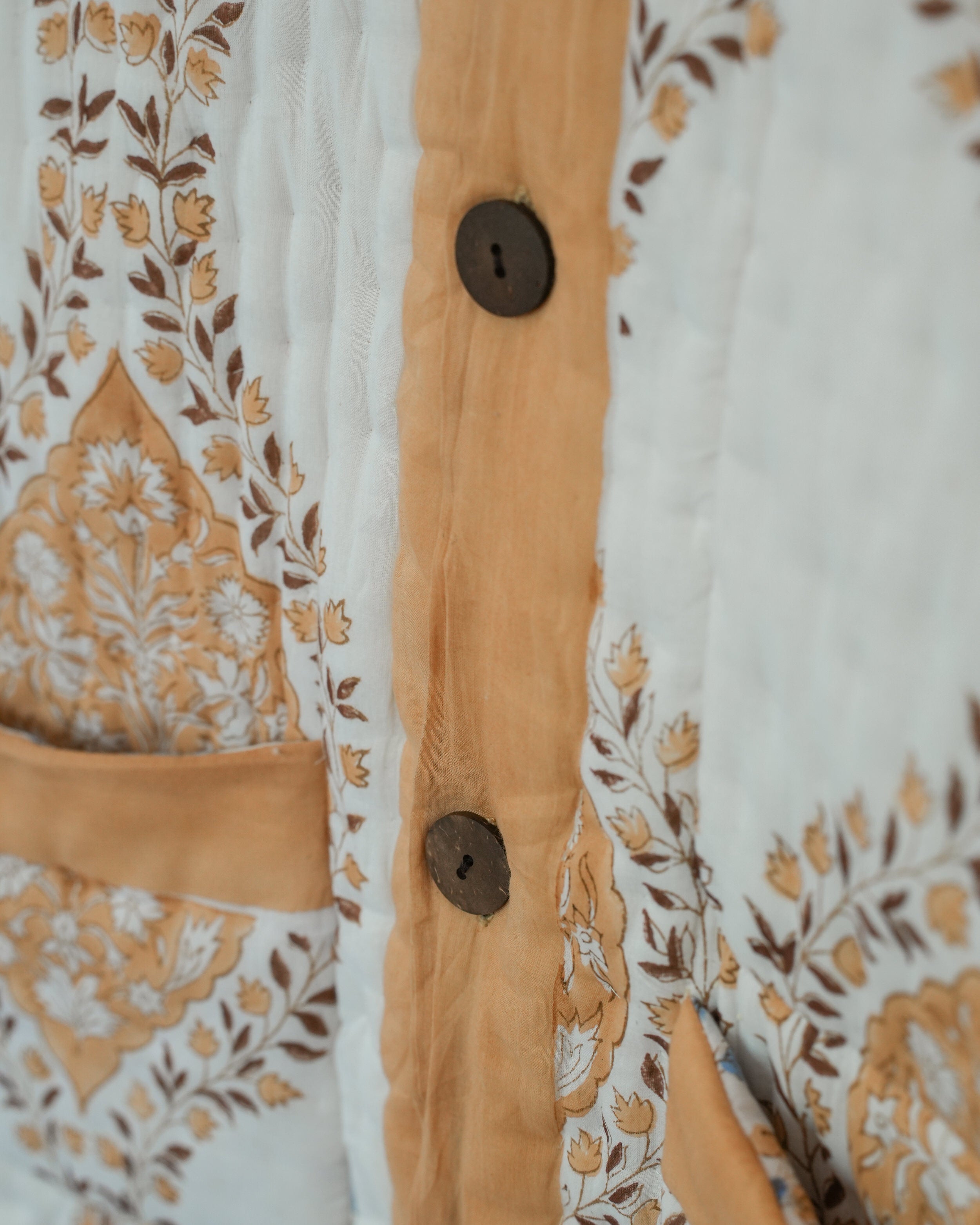Detail of front button placket on tan-trimmed quilted jacket with floral blockprint and coconut button