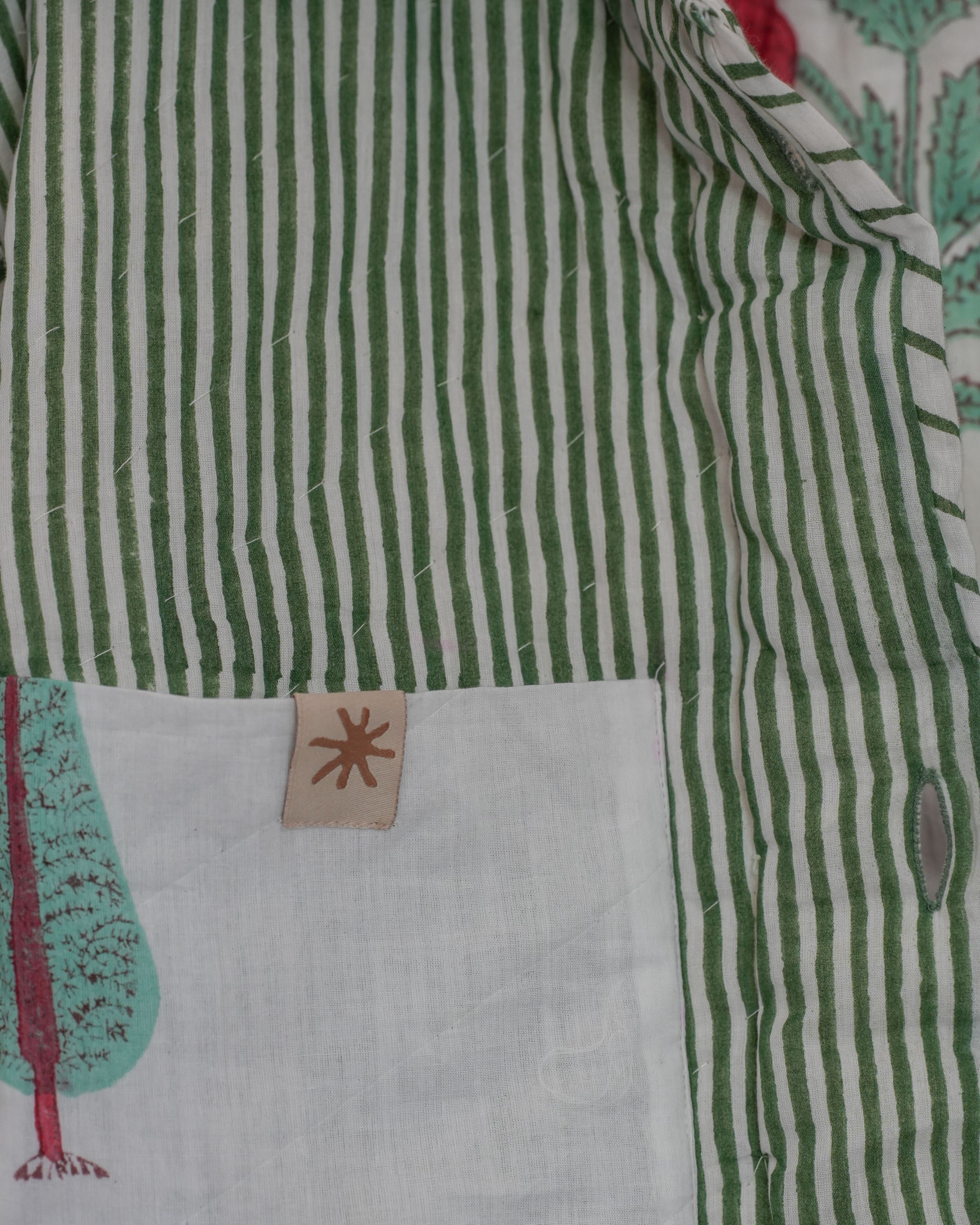Close-up of reversible quilted cotton jacket interior with green hand blockprinted stripes and label tag detail on pocket