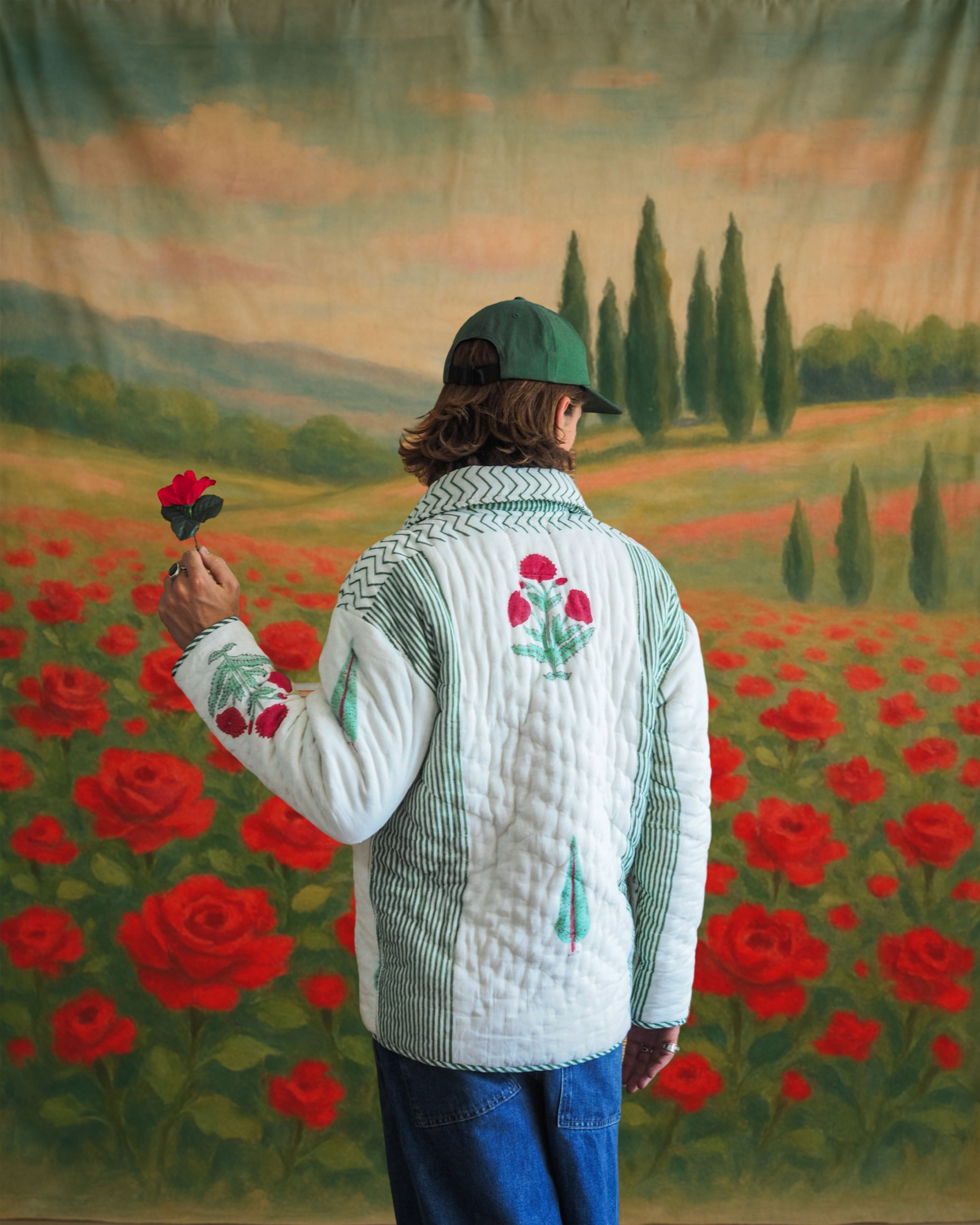 Model facing backward in reversible quilted cotton jacket with hand blockprinted floral motifs, holding a red flower