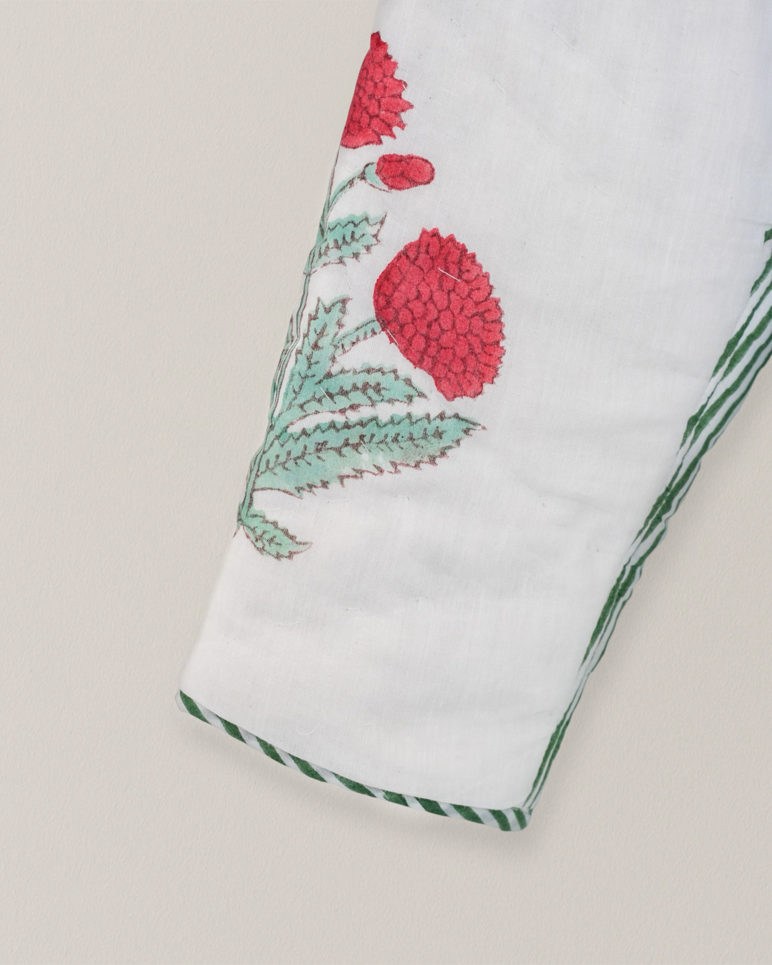 Close-up of quilted cotton sleeve with red floral blockprint and green hand-stitched detailing on white background