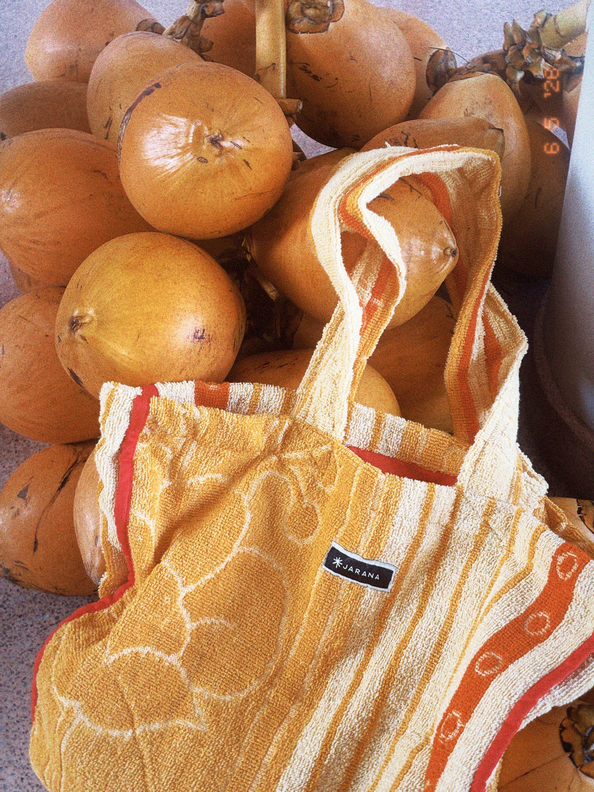 Yellow tote bag made from an upcycled Sri Lankan towel, photographed in front of thambili coconuts, showing its soft striped texture and relaxed shape